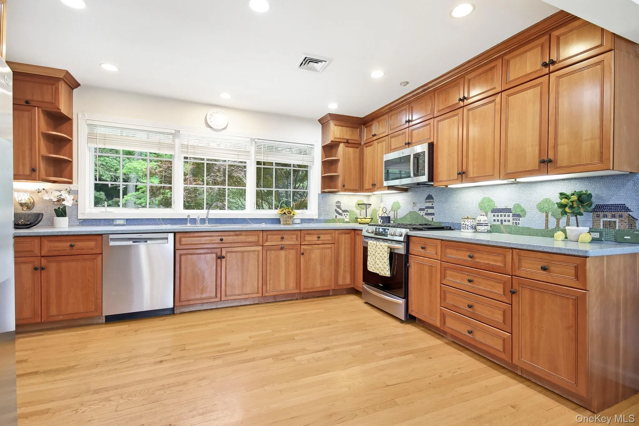 Kitchen featuring wood cabinetry, stainless steel appliances, hardwood flooring, recessed lighting, and a window overlooking exterior greenery Kitchen featuring wood cabinetry, stainless steel appliances, hardwood flooring, recessed lighting, and a window overlooking exterior greenery