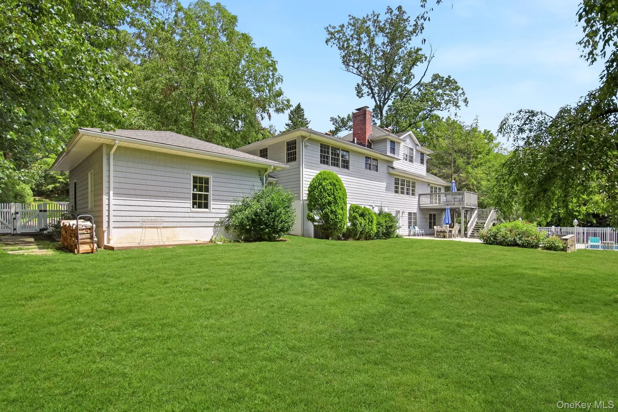 Expansive rear yard featuring a large green lawn, a multi-level deck, a fenced-in pool area, mature trees, and a detached back home structure with siding Expansive rear yard featuring a large green lawn, a multi-level deck, a fenced-in pool area, mature trees, and a detached back home structure with siding