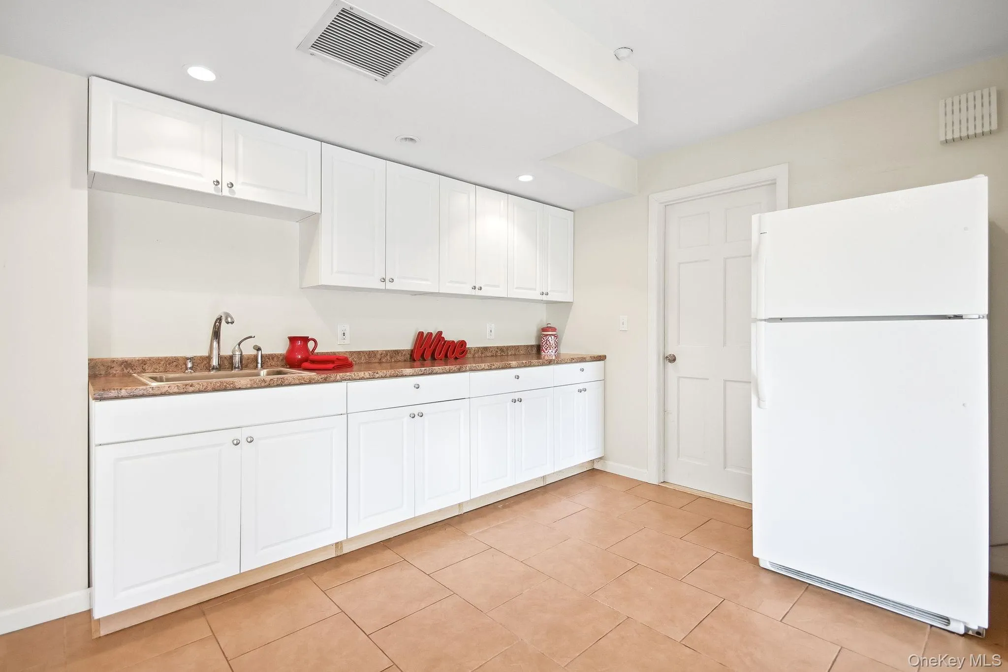 Kitchenette featuring white cabinetry, light-toned countertops, a stainless steel sink, and tile flooring Kitchenette featuring white cabinetry, light-toned countertops, a stainless steel sink, and tile flooring