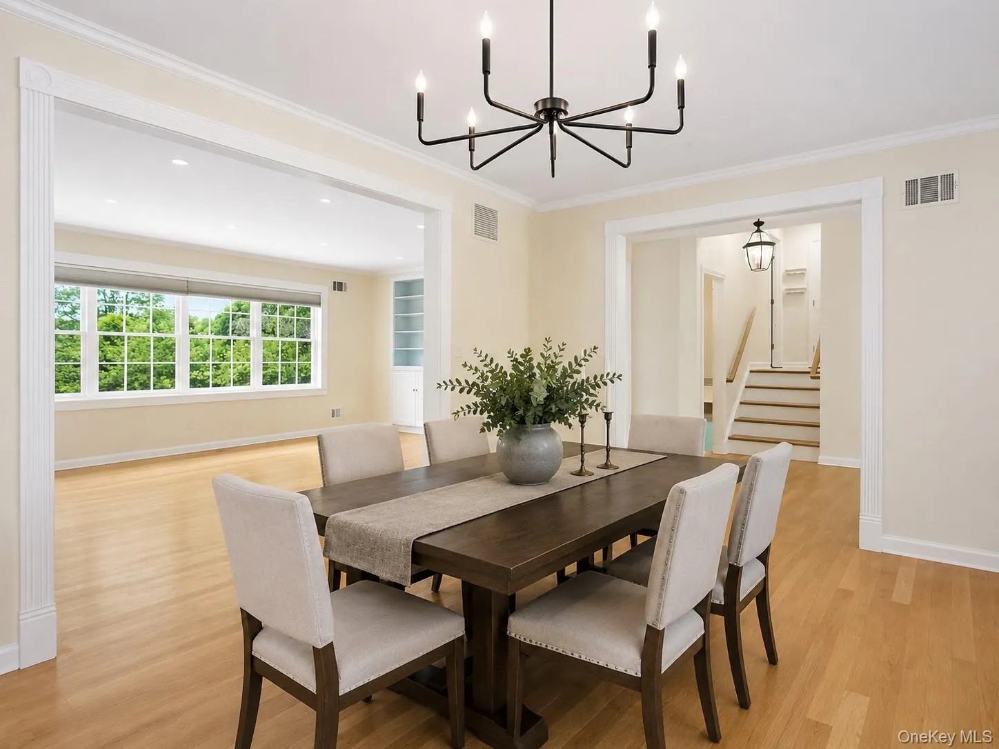 Dining area featuring a modern black chandelier, light hard wood flooring, and crown molding; open flow to the living room and kitchen Dining area featuring a modern black chandelier, light hard wood flooring, and crown molding; open flow to the living room and kitchen