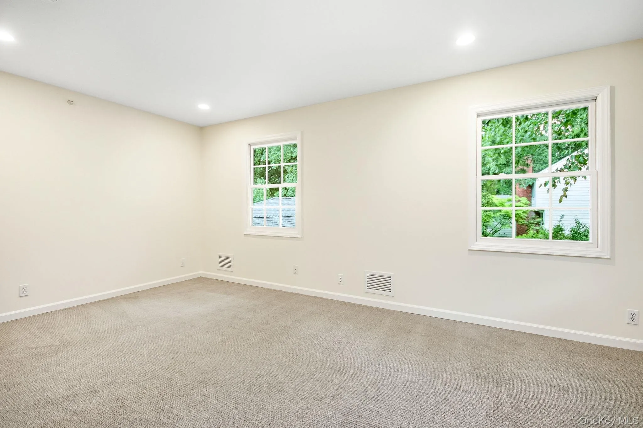Second en-suite bedroom featuring two windows with white trim, recessed lighting, neutral wall paint, and beige carpeting Second en-suite bedroom featuring two windows with white trim, recessed lighting, neutral wall paint, and beige carpeting