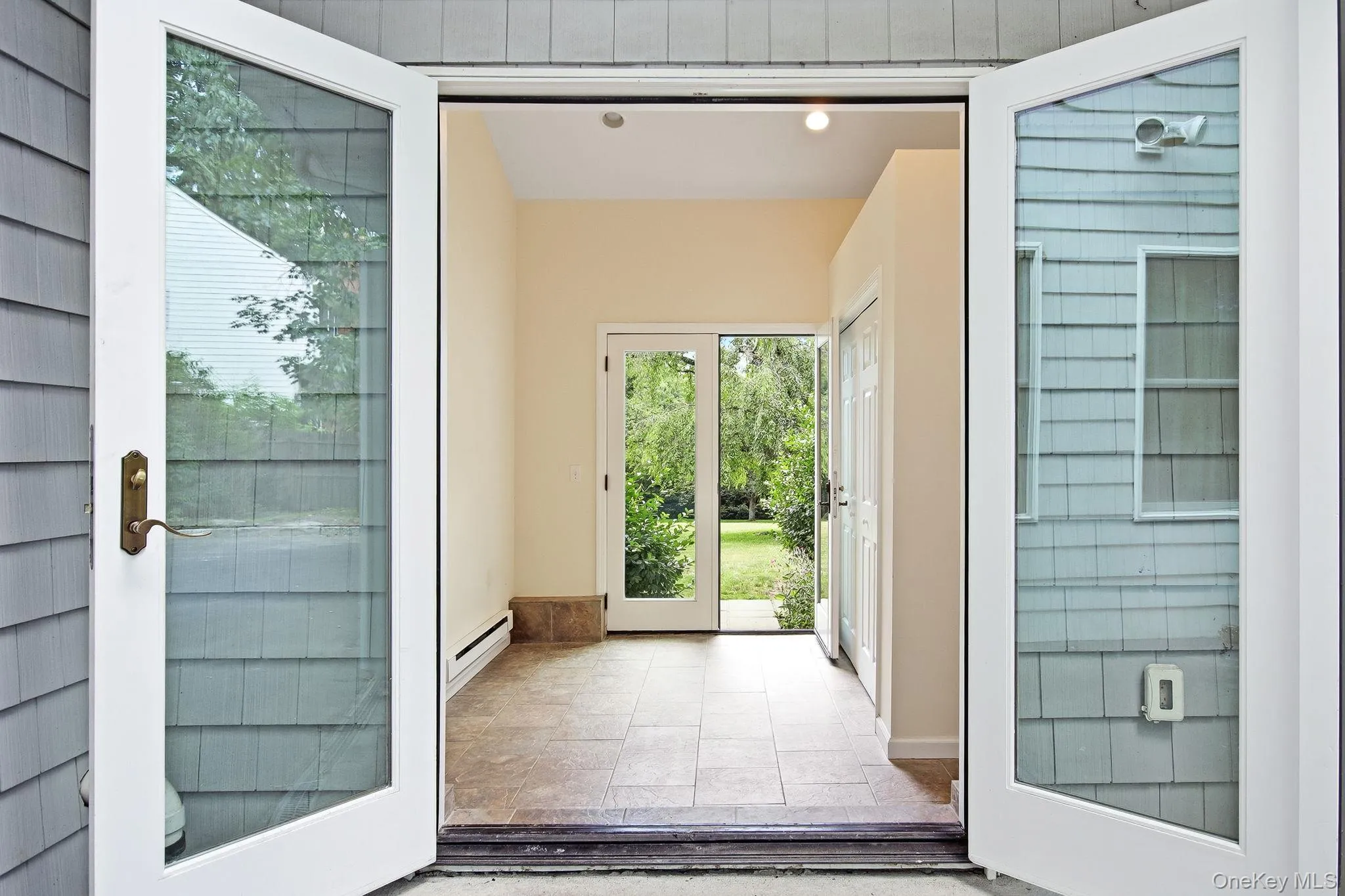 Breezway connecting the garage to the home and front yard to the back; exterior entry featuring white French doors opening into a tiled interior space Breezway connecting the garage to the home and front yard to the back; exterior entry featuring white French doors opening into a tiled interior space