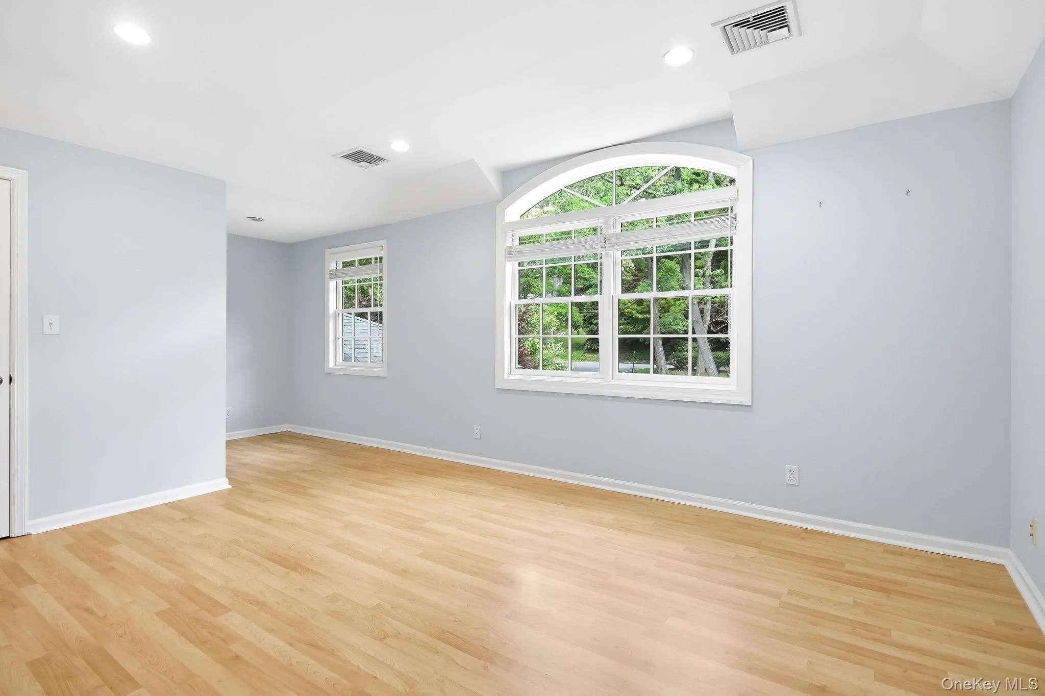 Upstairs Bedroom #3: Spacious room with wood-finish flooring, light blue walls, and a large arched window Upstairs Bedroom #3: Spacious room with wood-finish flooring, light blue walls, and a large arched window