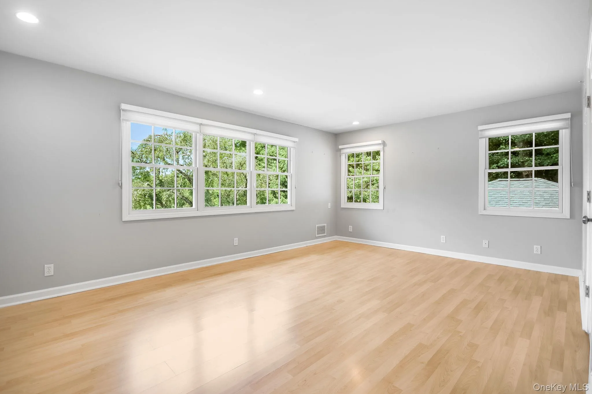 Primary en-suite (split level up); bright room featuring extensive natural light from multiple windows, recessed ceiling lighting, light wood-finish flooring, and light gray walls. Primary en-suite (split level up); bright room featuring extensive natural light from multiple windows, recessed ceiling lighting, light wood-finish flooring, and light gray walls.