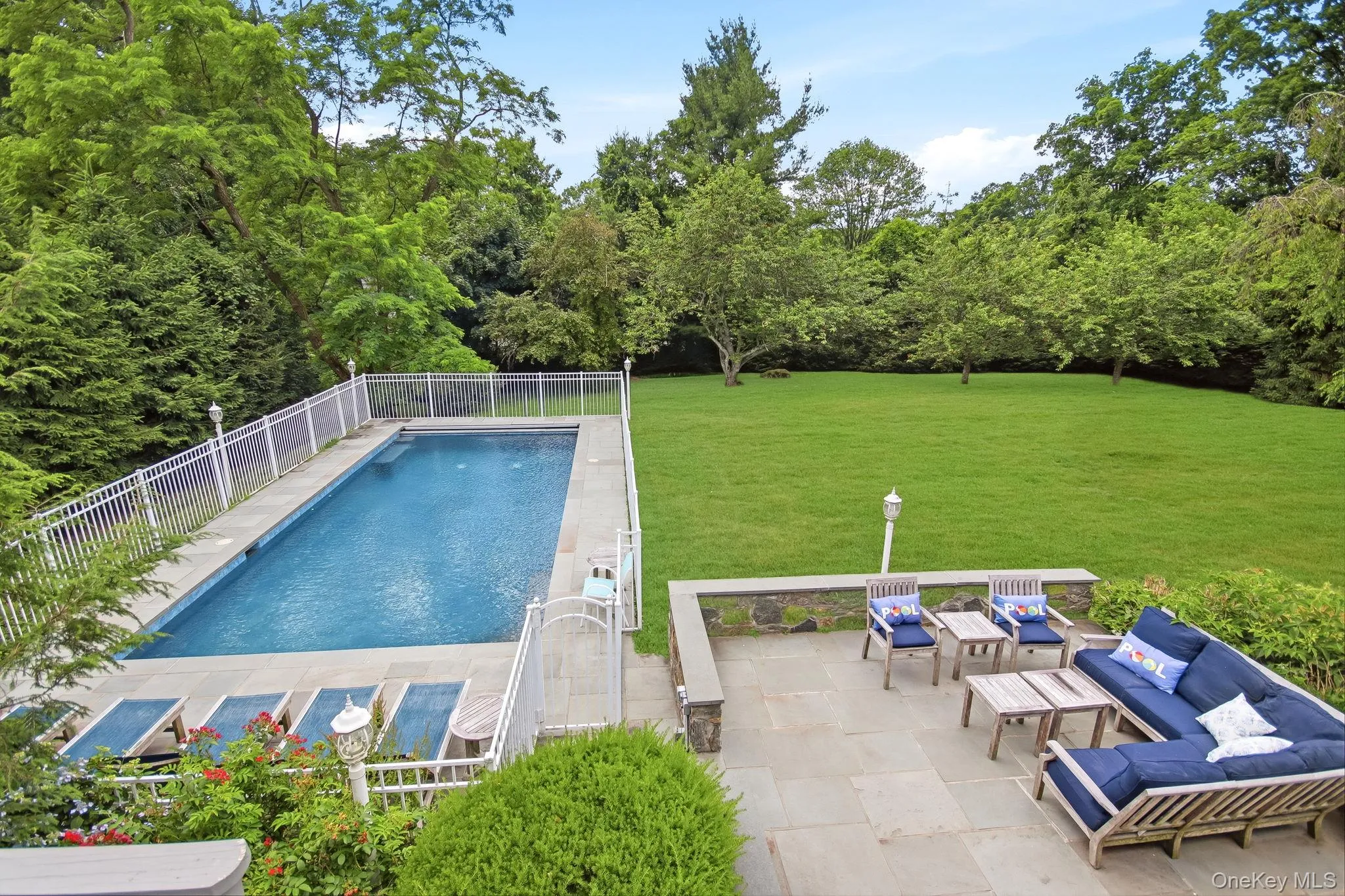 Outdoor entertaining space featuring a rectangular swimming pool with safety fencing, a stone patio, and an expansive lawn area Outdoor entertaining space featuring a rectangular swimming pool with safety fencing, a stone patio, and an expansive lawn area