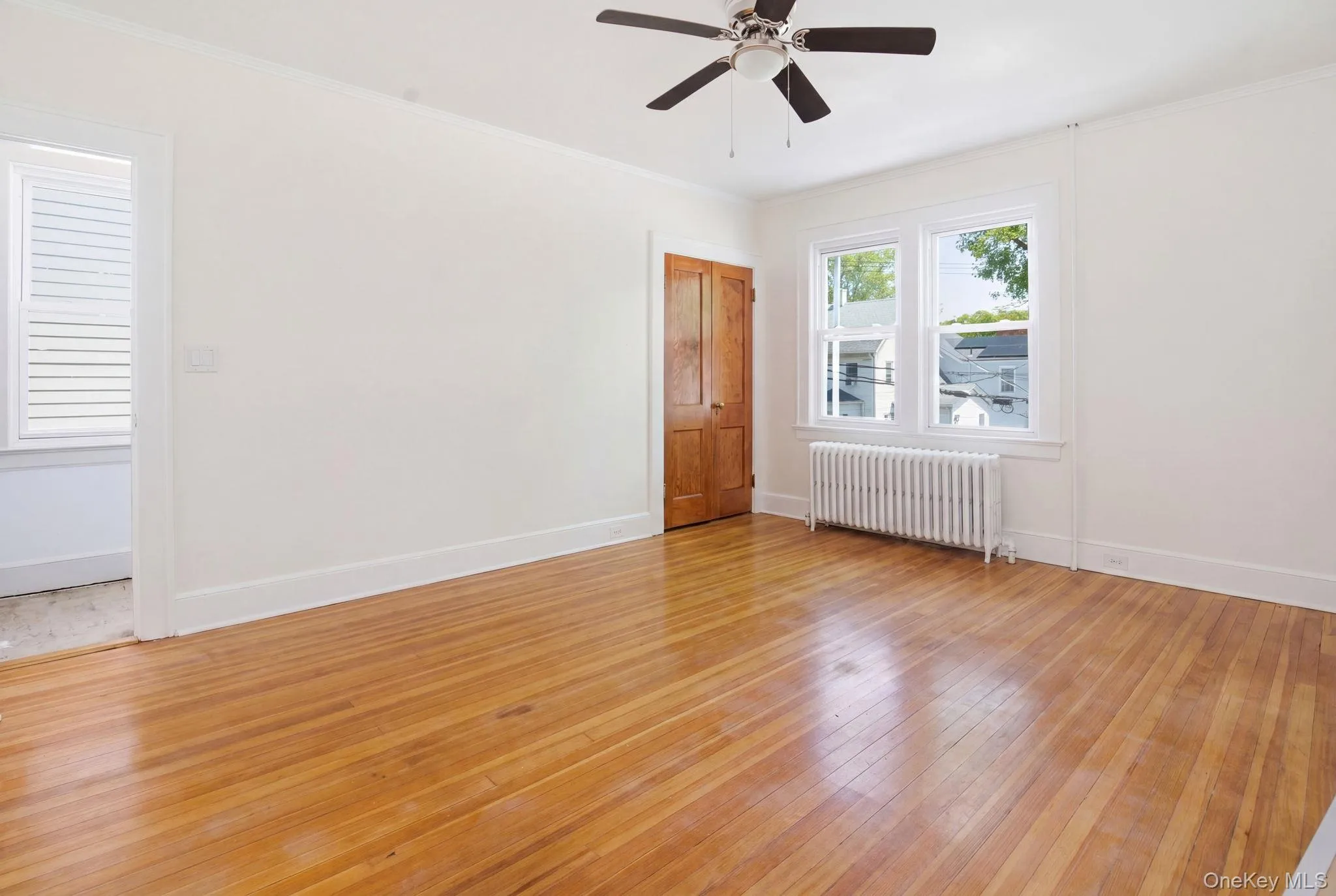 Bright room featuring wood-finish flooring, white walls, and a ceiling fan Bright room featuring wood-finish flooring, white walls, and a ceiling fan