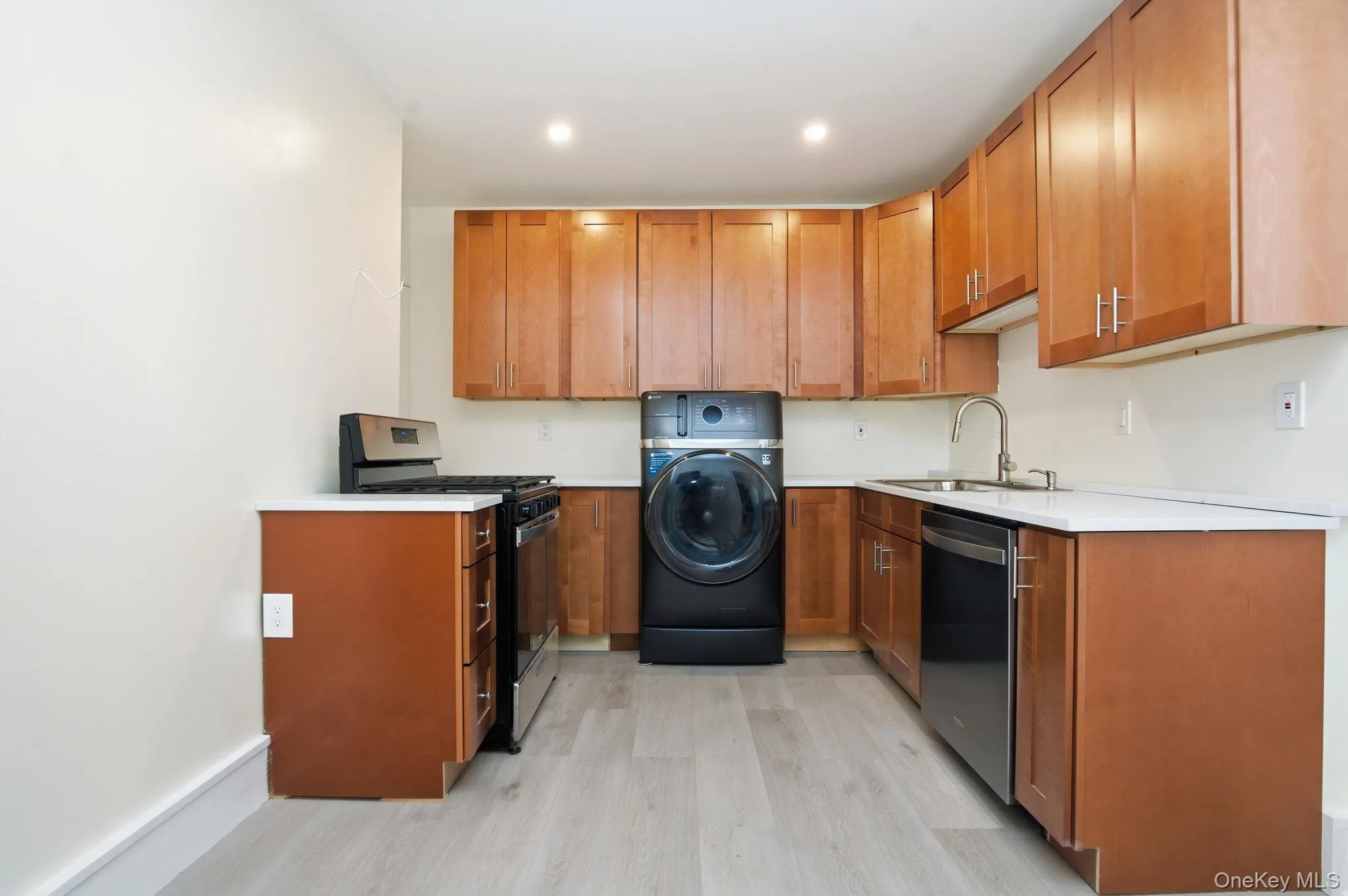 U-shaped kitchen featuring wood cabinetry with brushed nickel hardware, light-toned quartz countertops, a stainless steel gas range, and a stainless steel sink with a pull-down faucet U-shaped kitchen featuring wood cabinetry with brushed nickel hardware, light-toned quartz countertops, a stainless steel gas range, and a stainless steel sink with a pull-down faucet