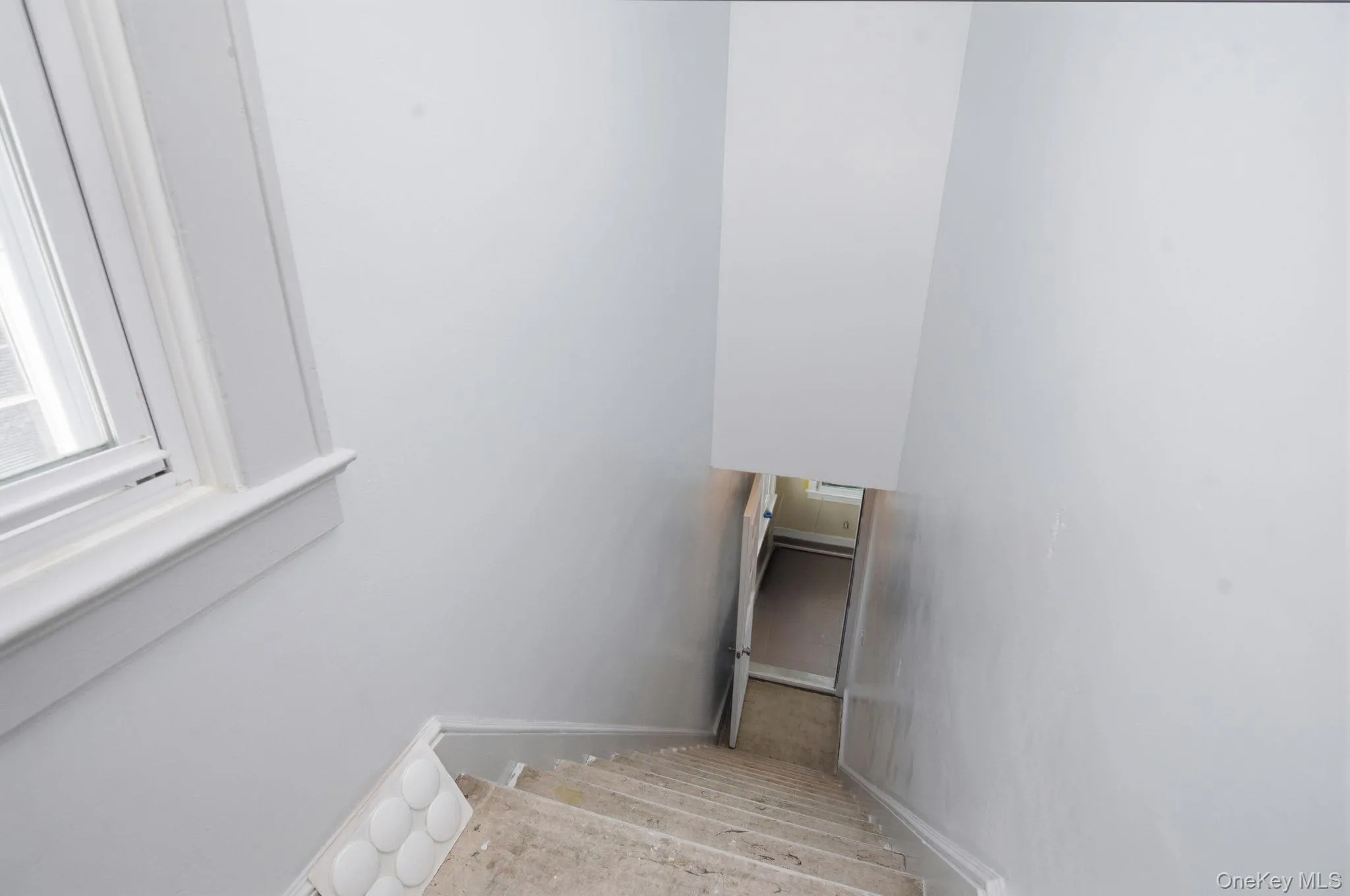 Stairwell featuring light-toned walls, a window with white trim, and a partial view of the entrance below. The carpet is going to be put on the stairs when entering the unit. Stairwell featuring light-toned walls, a window with white trim, and a partial view of the entrance below. The carpet is going to be put on the stairs when entering the unit.