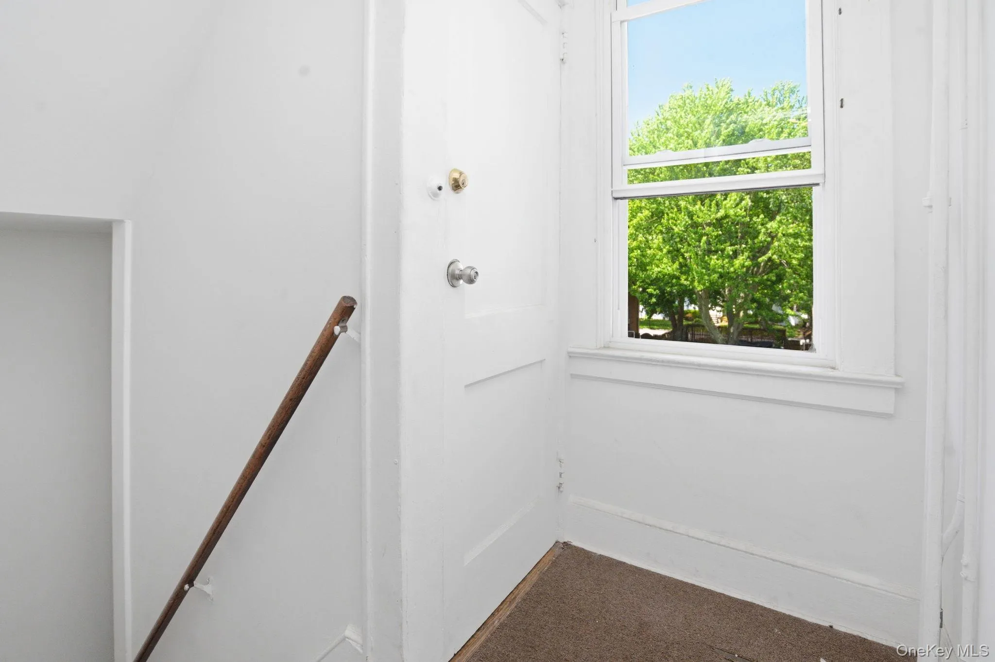 Entryway featuring a white paneled door, a single-hung window with white trim, and a wood handrail Entryway featuring a white paneled door, a single-hung window with white trim, and a wood handrail