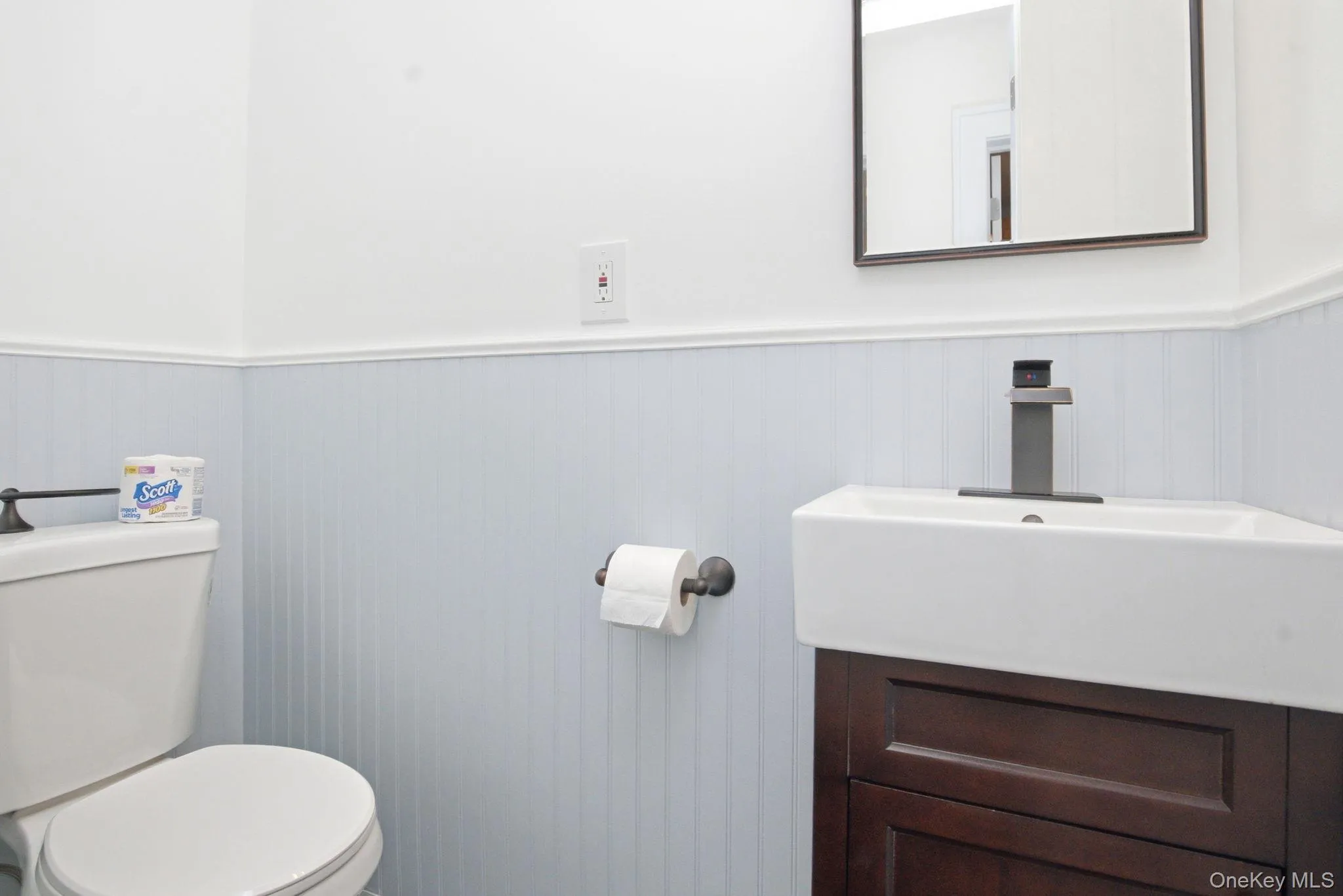 Bathroom featuring beadboard wainscoting, a corner vanity with a rectangular basin, and a modern single-handle faucet. This image depicts one half of the bathroom. Bathroom featuring beadboard wainscoting, a corner vanity with a rectangular basin, and a modern single-handle faucet. This image depicts one half of the bathroom.