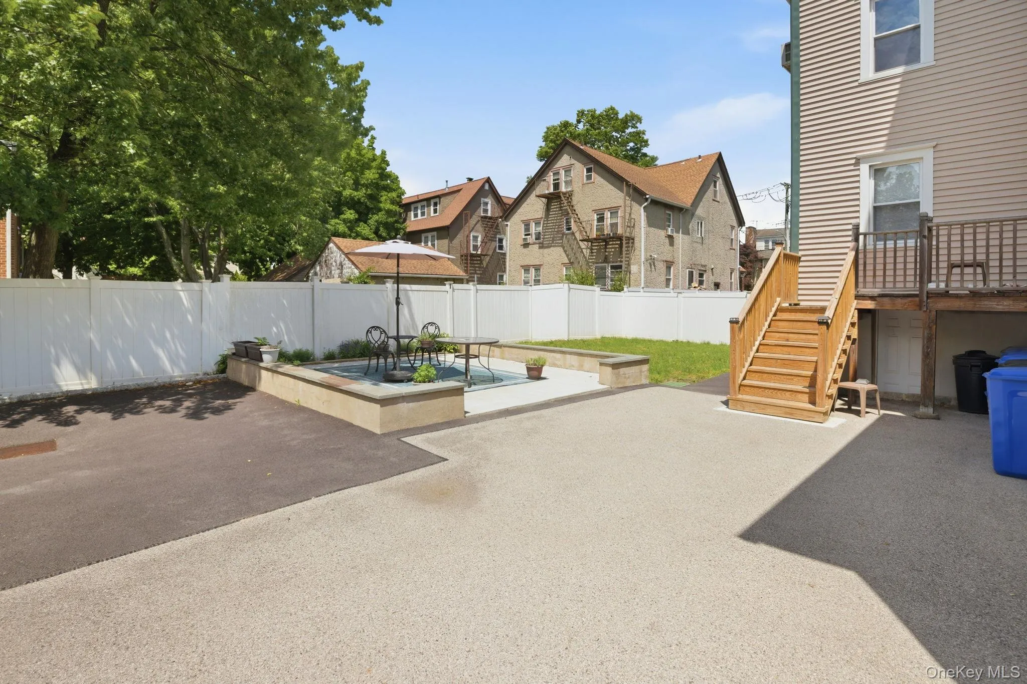 Expansive outdoor area featuring varied paving, a raised hardscape planter, and a private perimeter fence Expansive outdoor area featuring varied paving, a raised hardscape planter, and a private perimeter fence