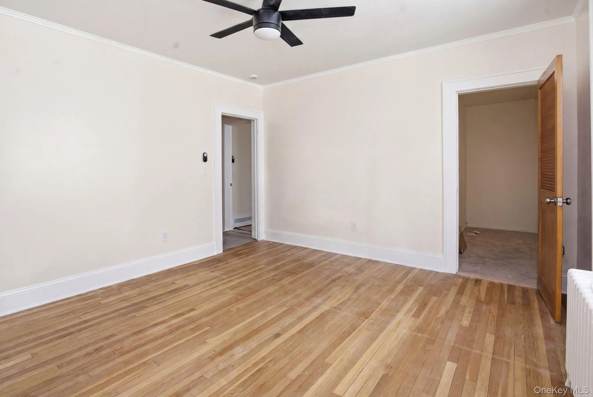 Spacious bedroom with oversized walk-in closet featuring hard-wood floors throughout, white baseboards, and a black ceiling fan with an integrated light kit Spacious bedroom with oversized walk-in closet featuring hard-wood floors throughout, white baseboards, and a black ceiling fan with an integrated light kit