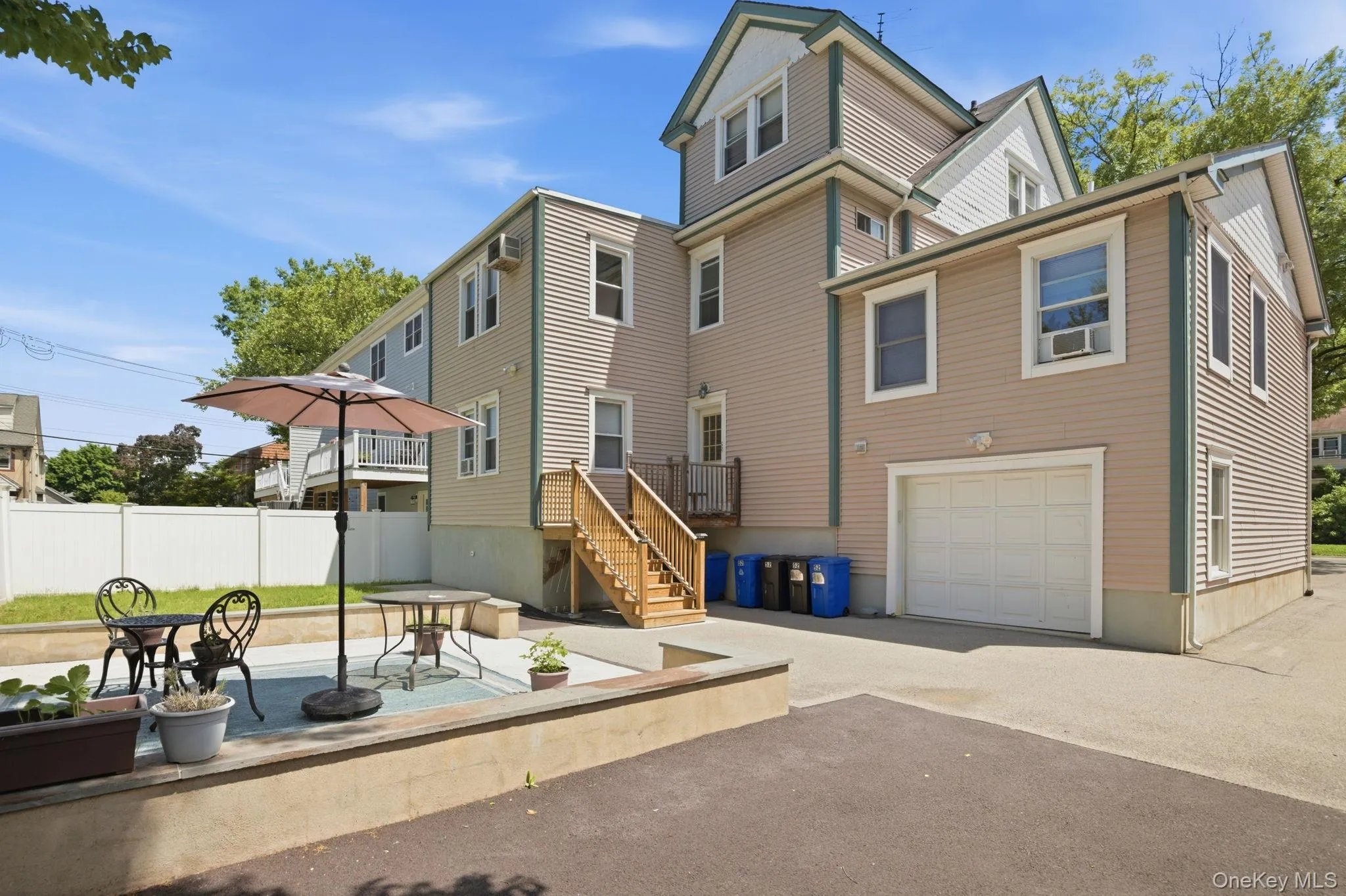 Rear exterior featuring light-toned siding, a white vinyl fence, and a garage with a white panel door. No garage parking. One assigned parking space. Rear exterior featuring light-toned siding, a white vinyl fence, and a garage with a white panel door. No garage parking. One assigned parking space.