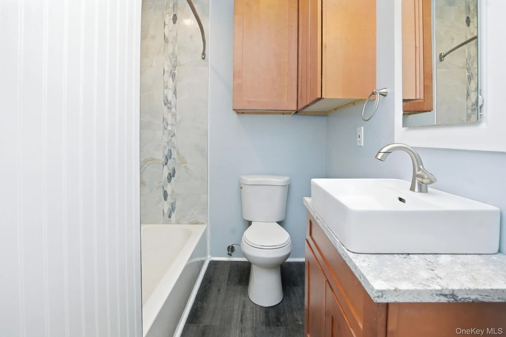 Bathroom featuring a vessel sink, wood-finish vanity with stone-finish countertop, and a tiled shower surround with accent mosaic Bathroom featuring a vessel sink, wood-finish vanity with stone-finish countertop, and a tiled shower surround with accent mosaic