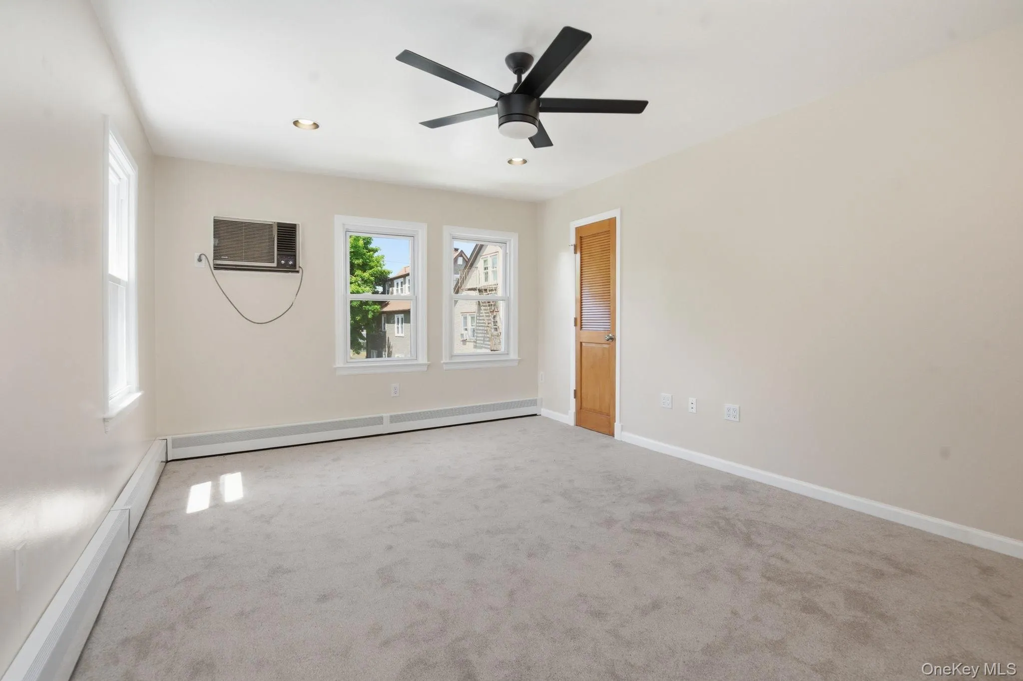 Oversized walk-in closet master bedroom facing the backyard featuring light-toned walls, neutral carpeting, and a dark-toned ceiling fan with integrated lighting Oversized walk-in closet master bedroom facing the backyard featuring light-toned walls, neutral carpeting, and a dark-toned ceiling fan with integrated lighting