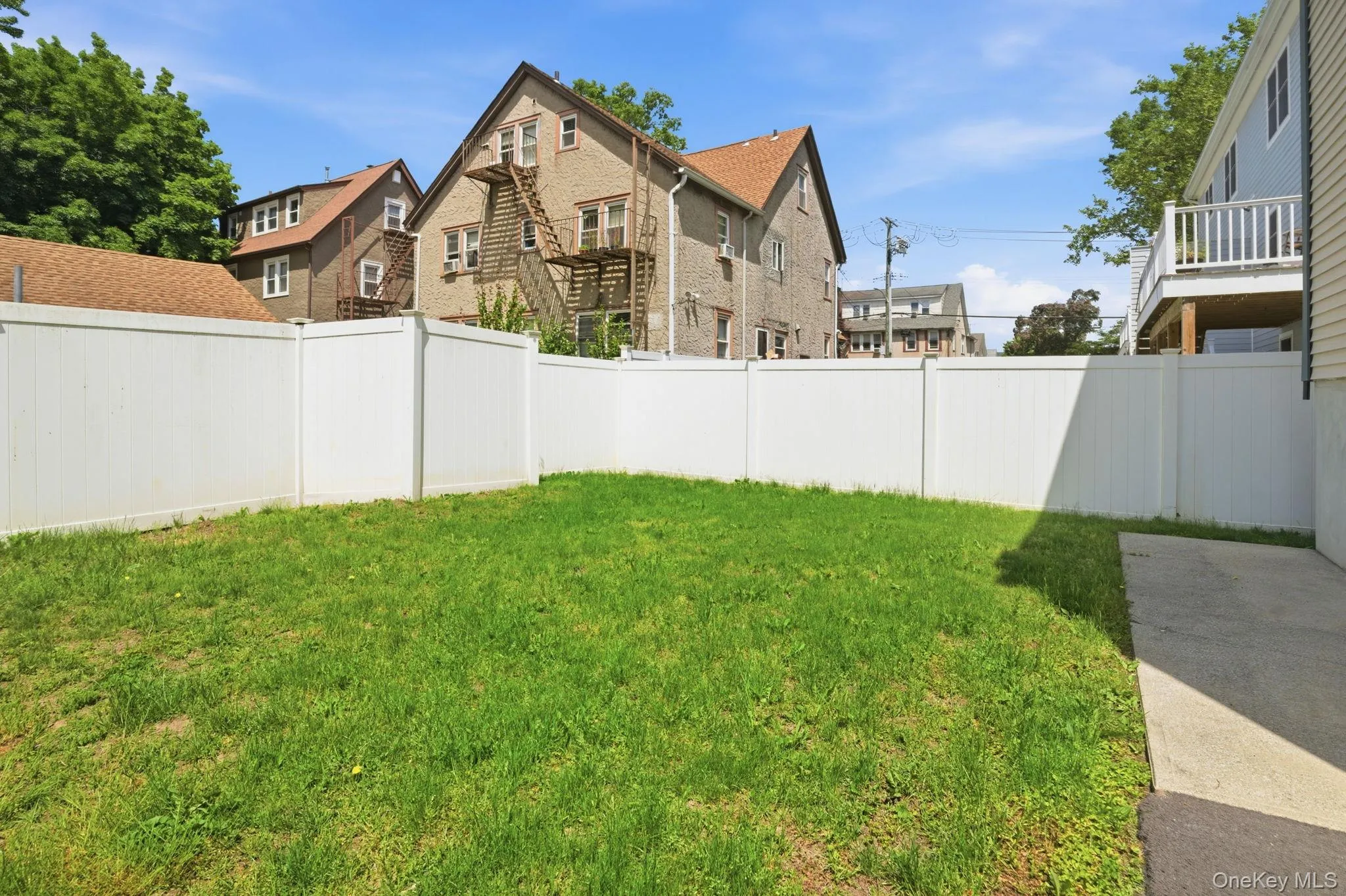 Manicured lawn area featuring a white privacy fence and a concrete patio Manicured lawn area featuring a white privacy fence and a concrete patio
