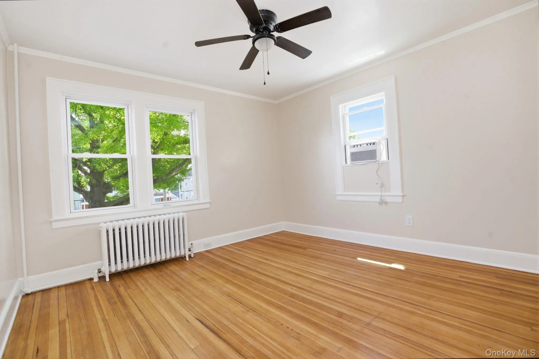 Room featuring hardwood flooring, a ceiling fan, crown molding, and baseboards Room featuring hardwood flooring, a ceiling fan, crown molding, and baseboards