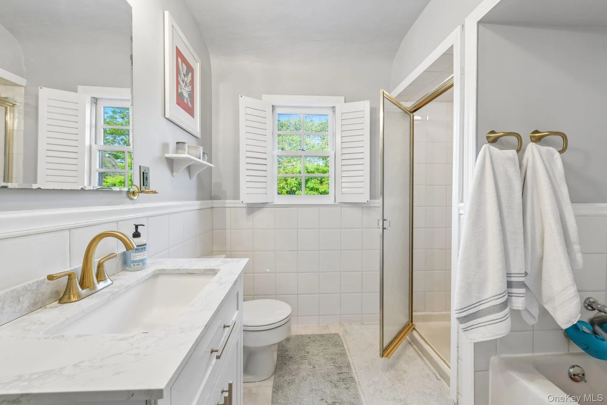 Bathroom featuring a white vanity with a light-colored countertop, a gold-toned faucet, and a large wall mirror Bathroom featuring a white vanity with a light-colored countertop, a gold-toned faucet, and a large wall mirror