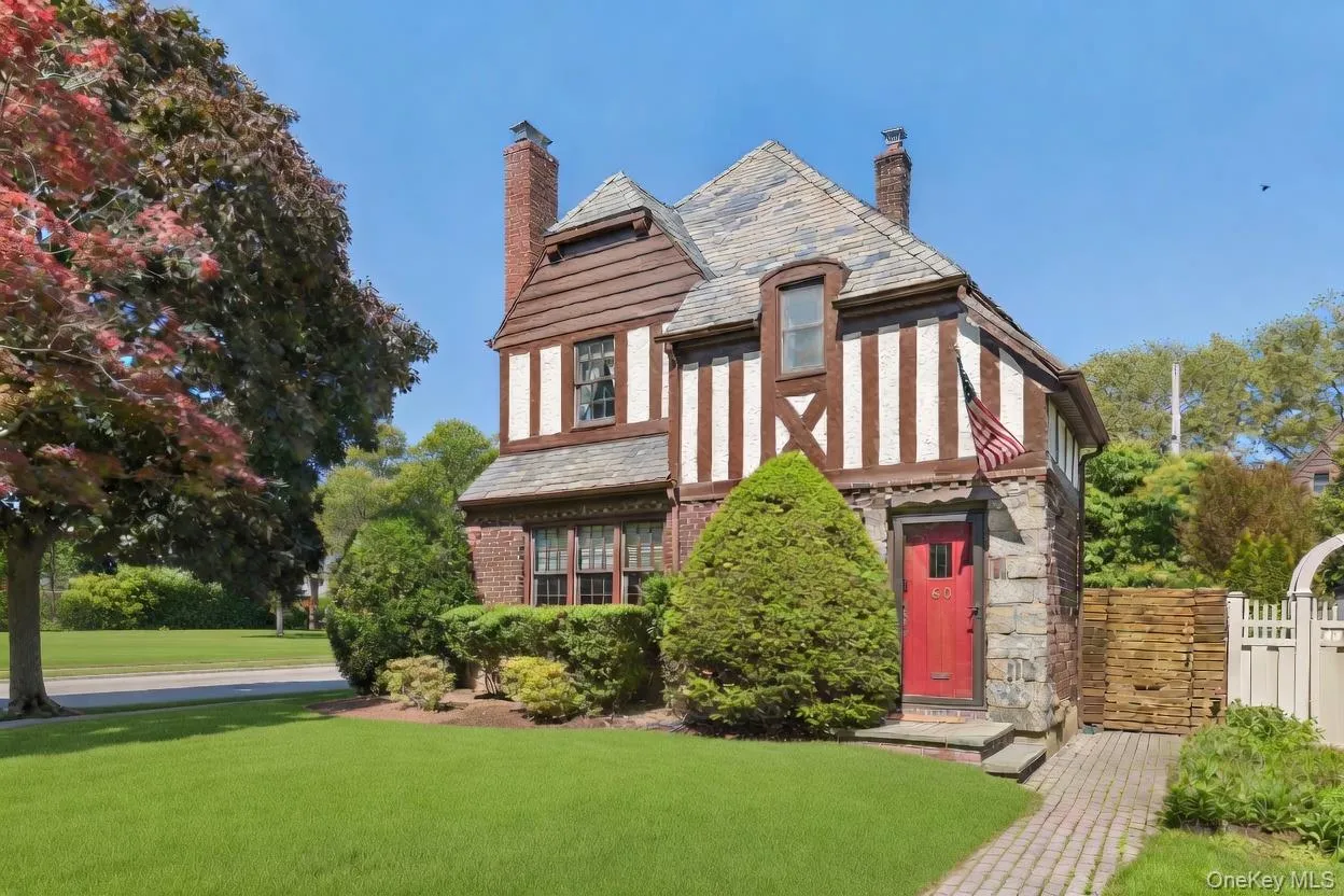 Tudor-style exterior featuring a red entry door, brick and stone cladding, decorative half-timbering, and a slate roof Tudor-style exterior featuring a red entry door, brick and stone cladding, decorative half-timbering, and a slate roof