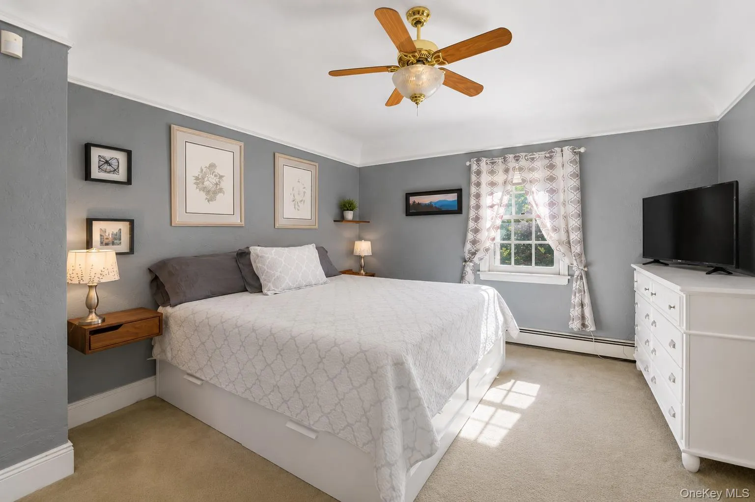 Carpeted room featuring a ceiling fan with light fixture, a window with trim, crown molding, and two wall-mounted floating shelves Carpeted room featuring a ceiling fan with light fixture, a window with trim, crown molding, and two wall-mounted floating shelves