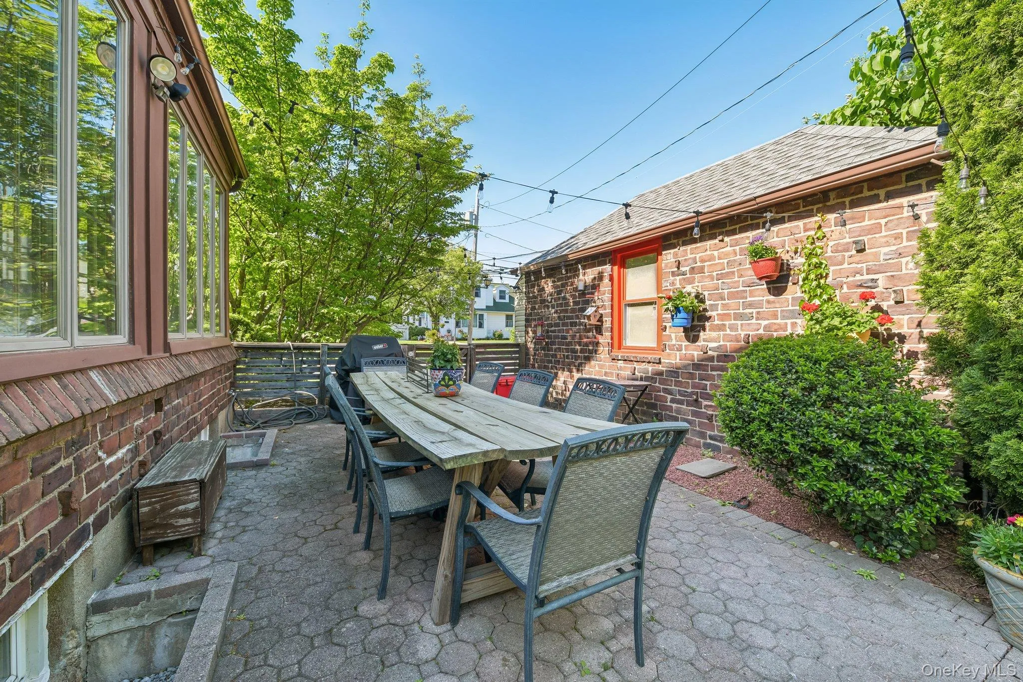 Paved patio featuring a brick exterior, extensive fenestration, and mature plantings Paved patio featuring a brick exterior, extensive fenestration, and mature plantings