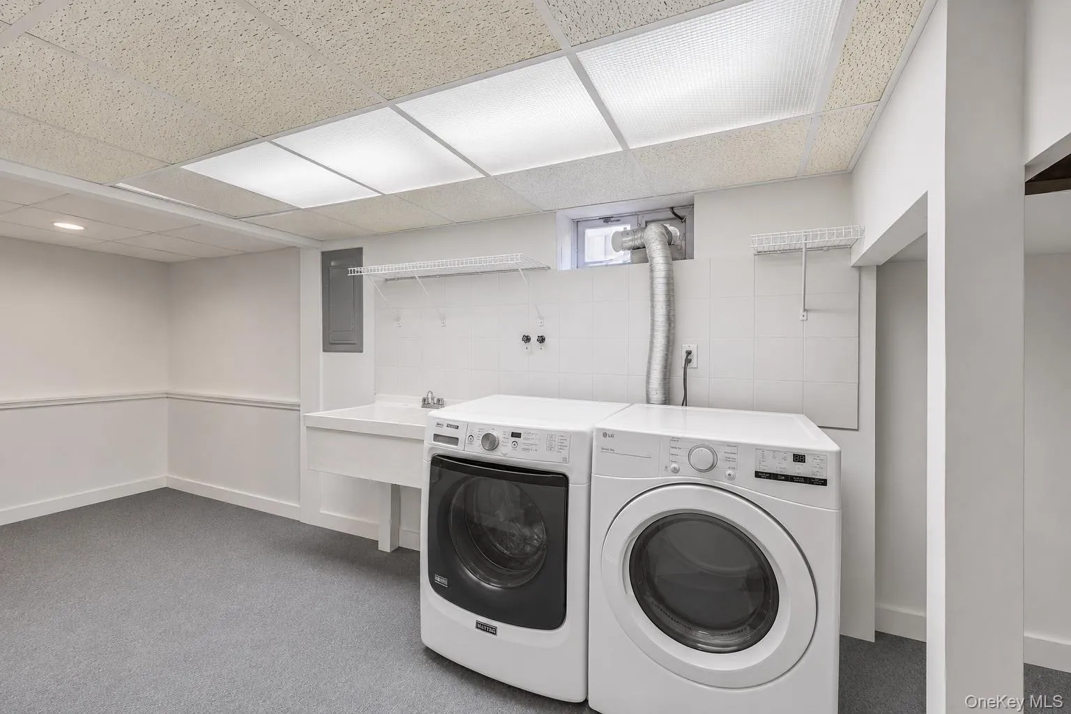 Dedicated laundry area featuring a utility sink, white tiled backsplash, and overhead wire shelving Dedicated laundry area featuring a utility sink, white tiled backsplash, and overhead wire shelving