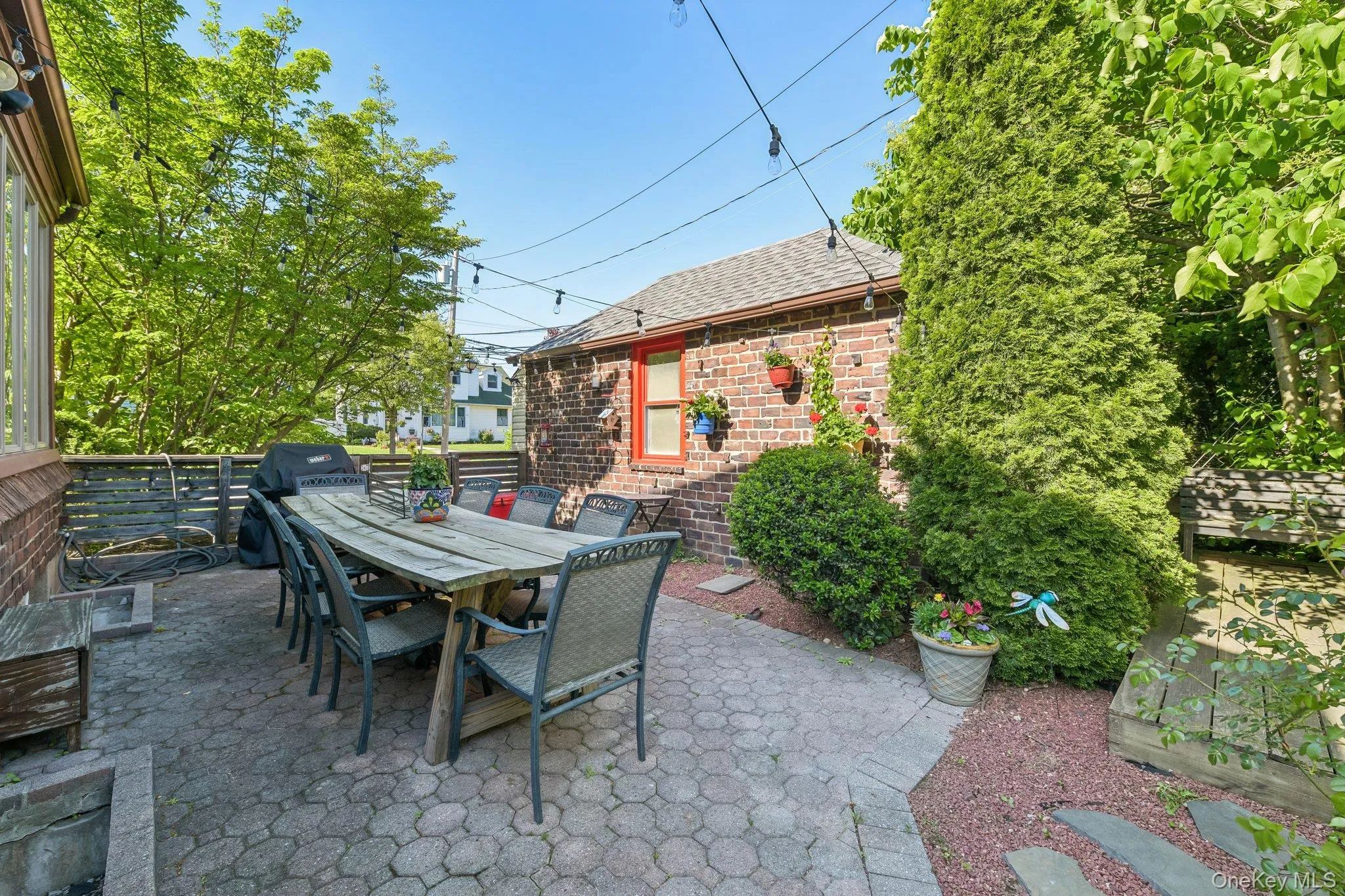 Paved patio area featuring decorative string lighting and a separate brick structure with a red-trimmed window Paved patio area featuring decorative string lighting and a separate brick structure with a red-trimmed window