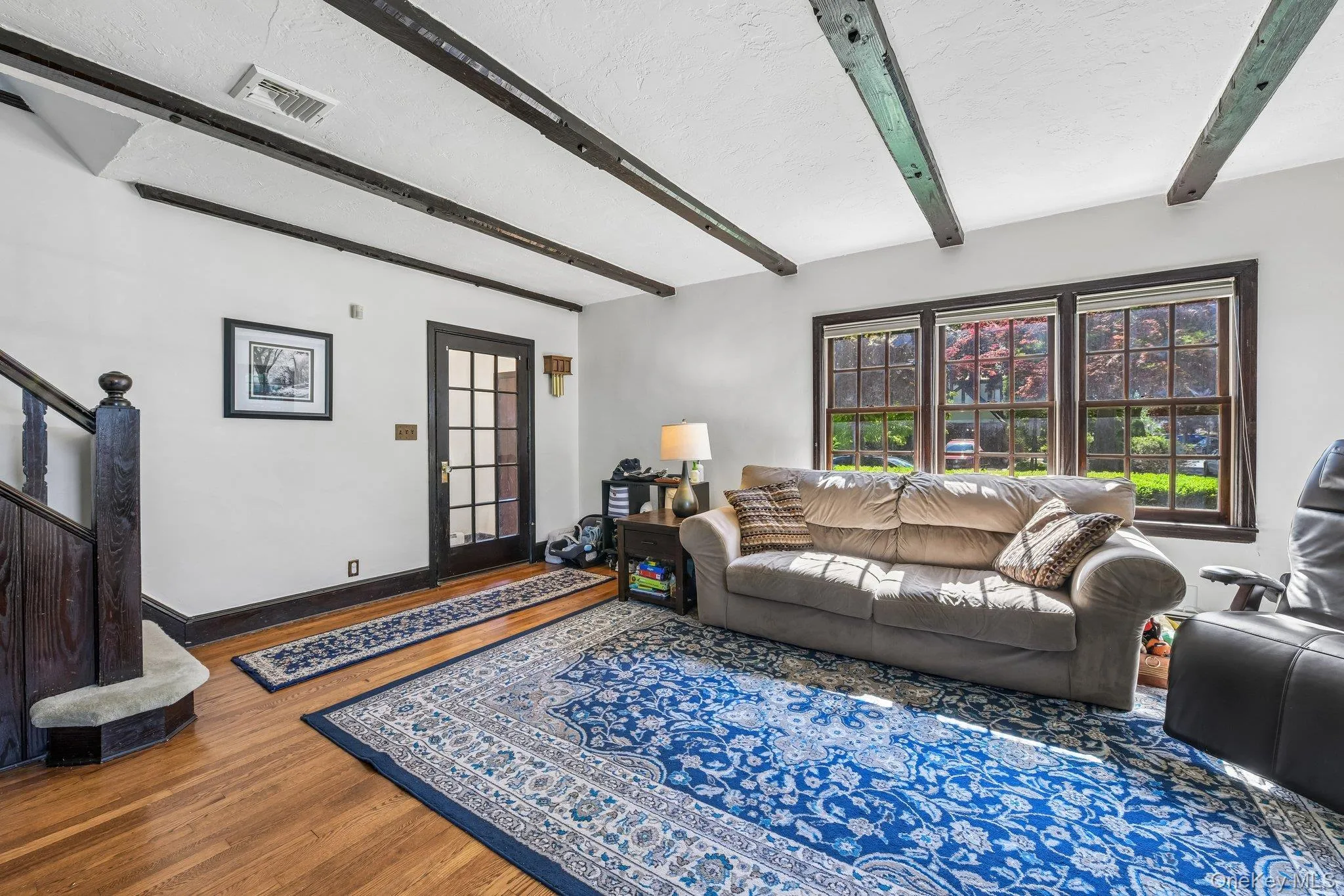 Living area featuring exposed ceiling beams, hardwood flooring, a multi-pane door, and a three-panel window Living area featuring exposed ceiling beams, hardwood flooring, a multi-pane door, and a three-panel window