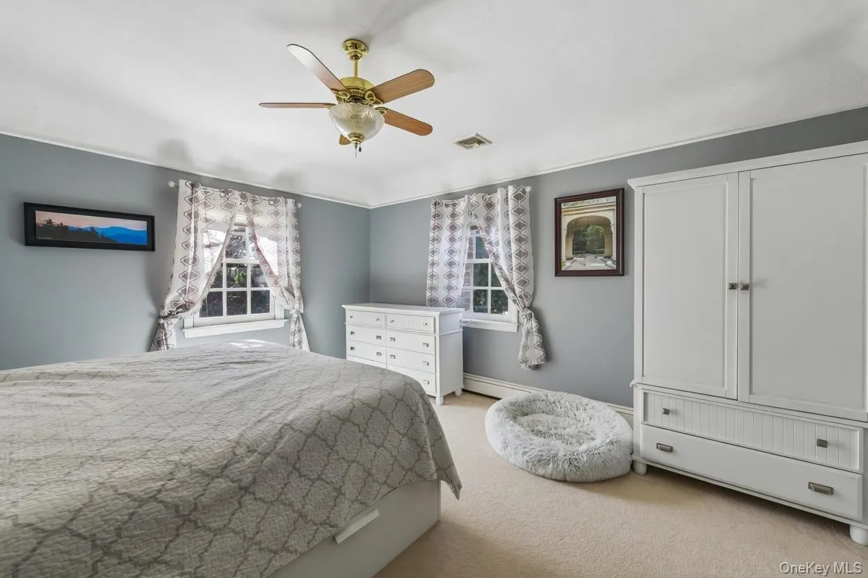 Carpeted room featuring a ceiling fan with integrated lighting, two windows with patterned curtains, and neutral wall paint Carpeted room featuring a ceiling fan with integrated lighting, two windows with patterned curtains, and neutral wall paint