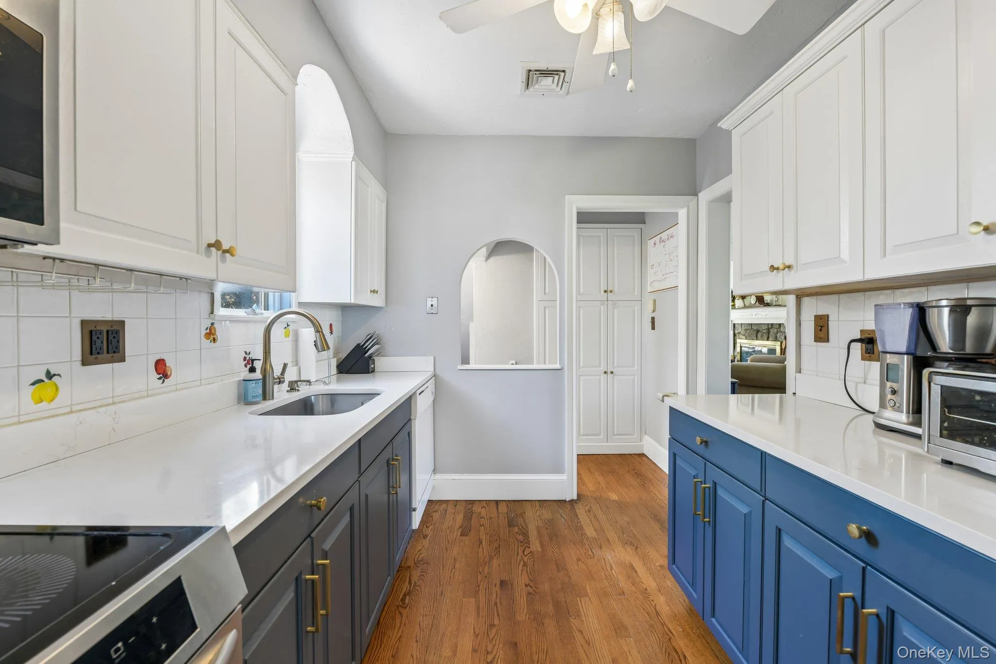 Galley kitchen with two-tone cabinetry, white countertops, stainless steel sink, and wood-finish flooring Galley kitchen with two-tone cabinetry, white countertops, stainless steel sink, and wood-finish flooring