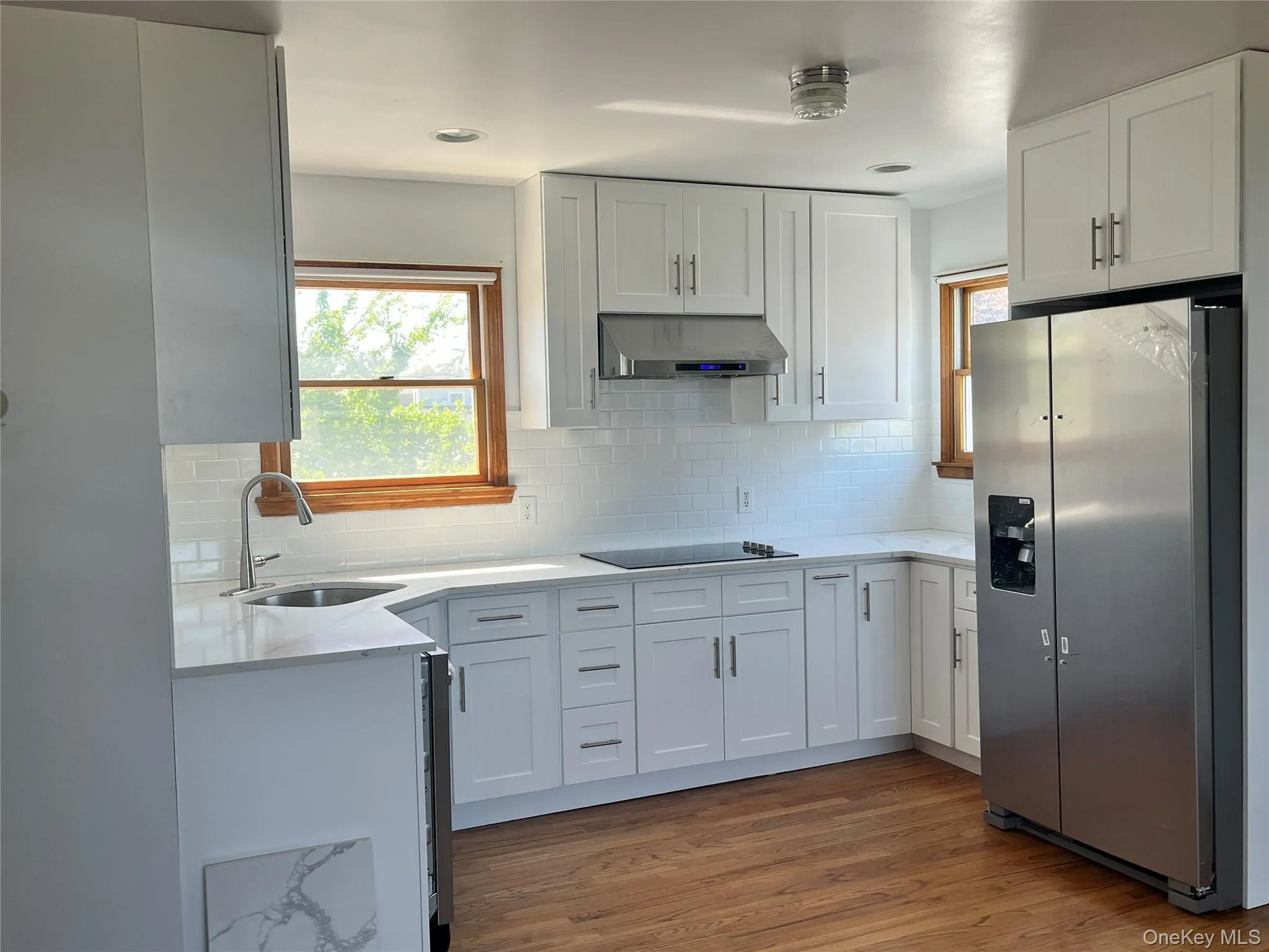 Modern kitchen featuring white shaker cabinetry, stainless steel appliances, a subway tile backsplash, and wood-finish flooring Modern kitchen featuring white shaker cabinetry, stainless steel appliances, a subway tile backsplash, and wood-finish flooring
