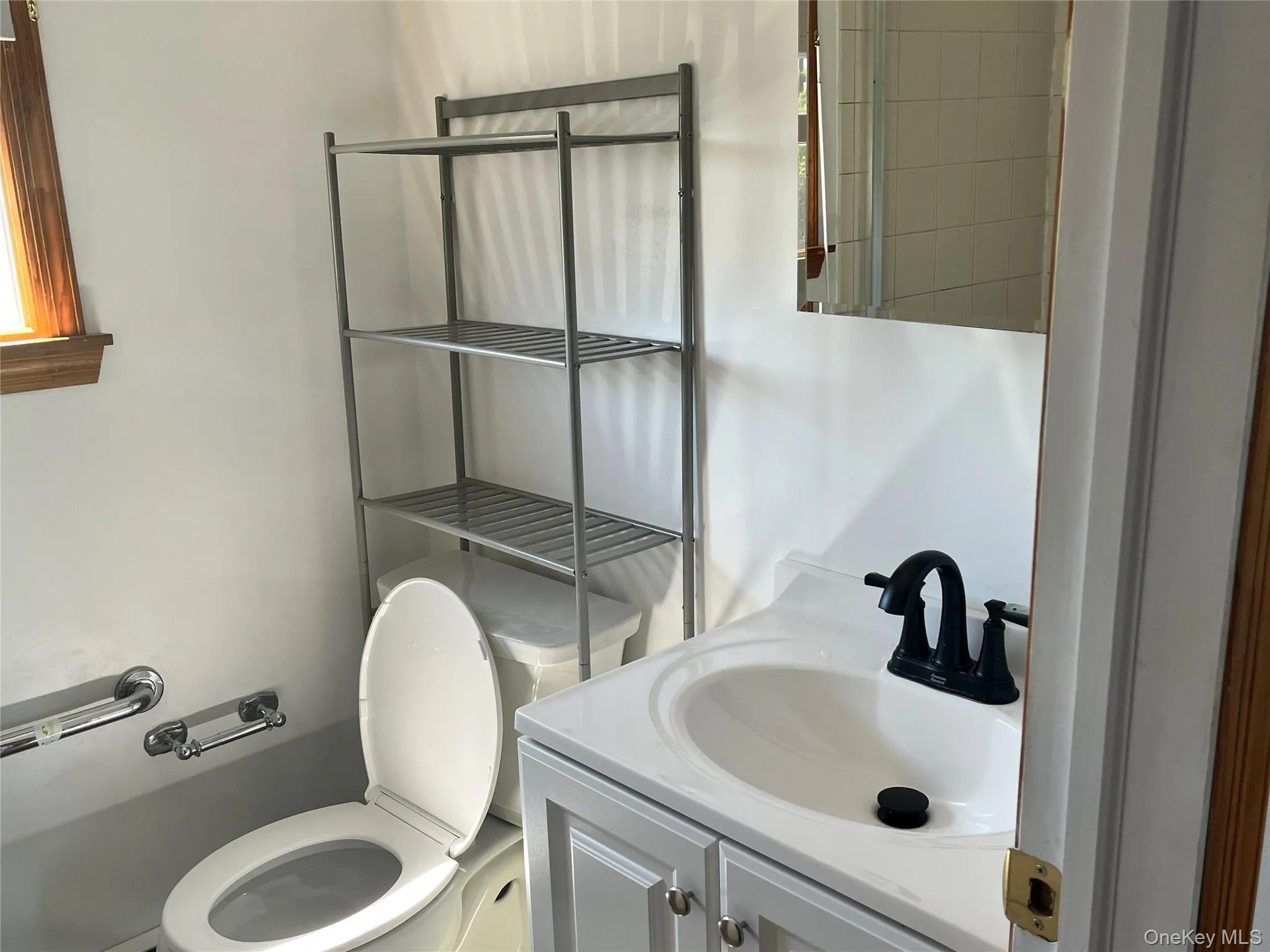 Bathroom featuring a white vanity with a dark faucet, mirror, toilet, and chrome grab bar Bathroom featuring a white vanity with a dark faucet, mirror, toilet, and chrome grab bar