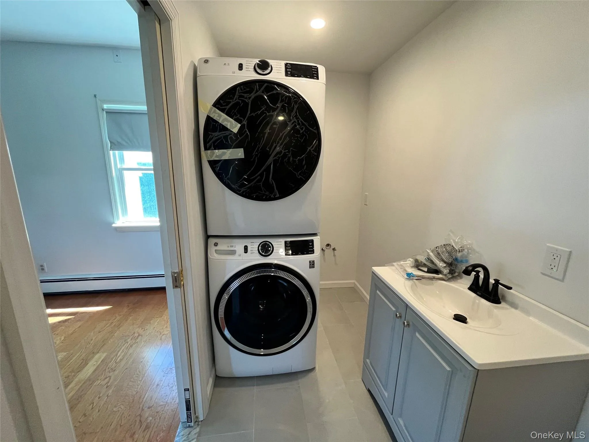 Dedicated laundry area featuring a stacked washer and dryer, recessed lighting, and a single vanity with a matte black faucet Dedicated laundry area featuring a stacked washer and dryer, recessed lighting, and a single vanity with a matte black faucet