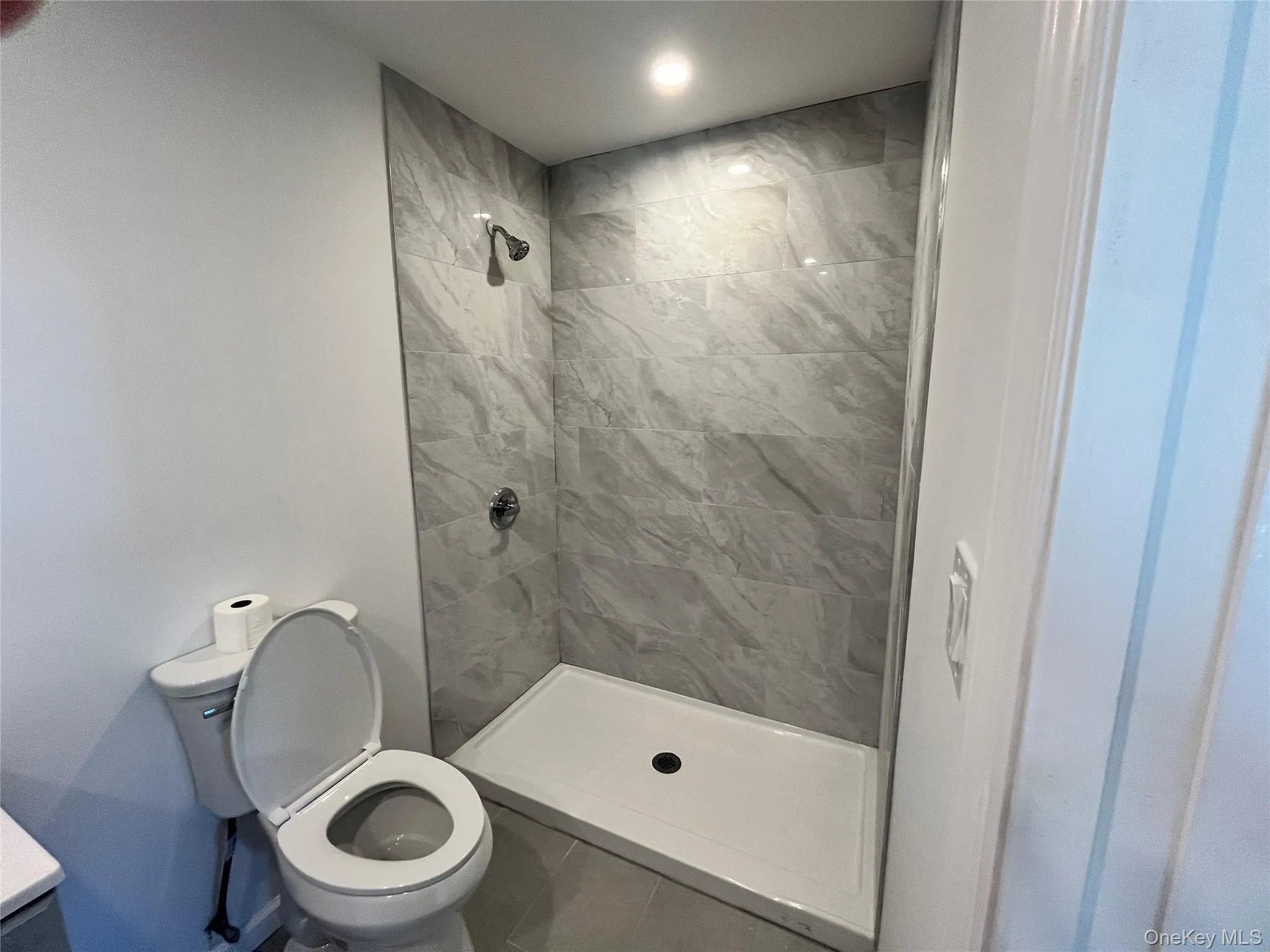 Modern bathroom featuring a walk-in shower with gray tile surround, chrome shower fixtures, and a white shower base Modern bathroom featuring a walk-in shower with gray tile surround, chrome shower fixtures, and a white shower base