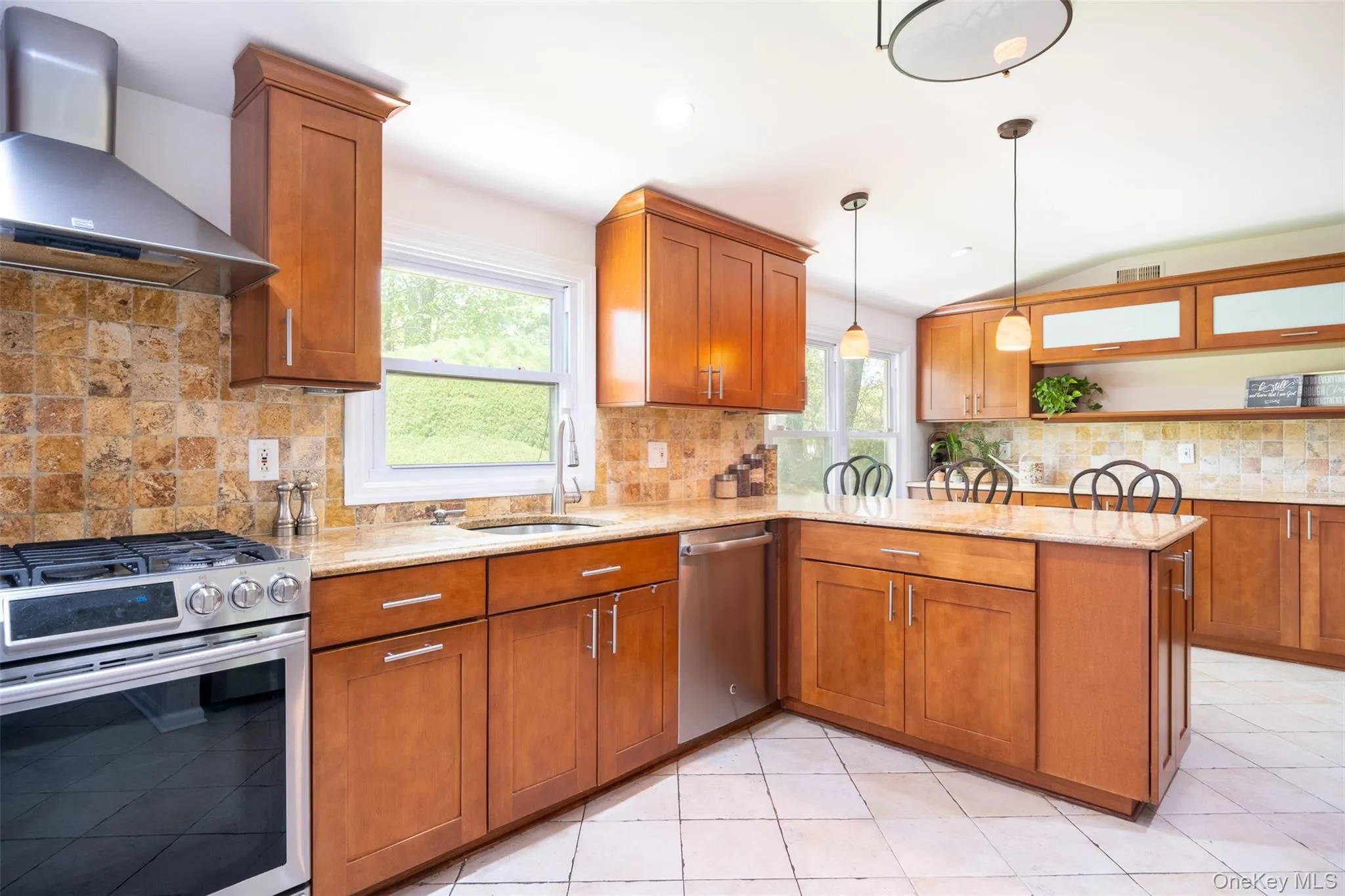 Kitchen with appliances with stainless steel finishes, wall chimney range hood, a sink, a peninsula, and brown cabinets Kitchen with appliances with stainless steel finishes, wall chimney range hood, a sink, a peninsula, and brown cabinets