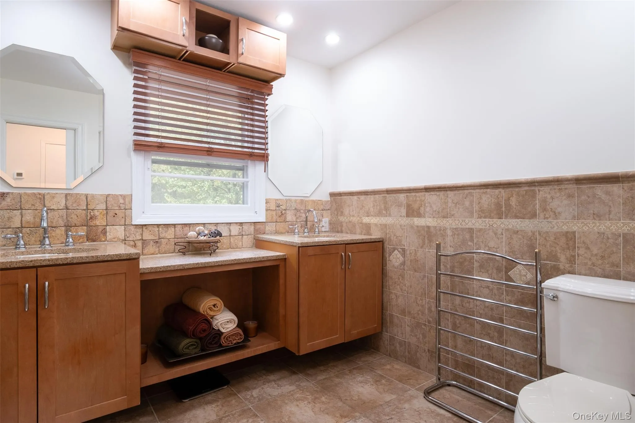 Full bath with tile walls, toilet, a wainscoted wall, two vanities, and tile patterned floors Full bath with tile walls, toilet, a wainscoted wall, two vanities, and tile patterned floors
