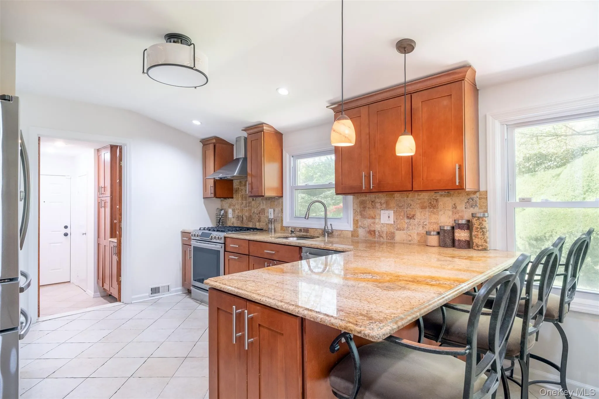 Kitchen with stainless steel appliances, a sink, wall chimney range hood, brown cabinets, and backsplash Kitchen with stainless steel appliances, a sink, wall chimney range hood, brown cabinets, and backsplash