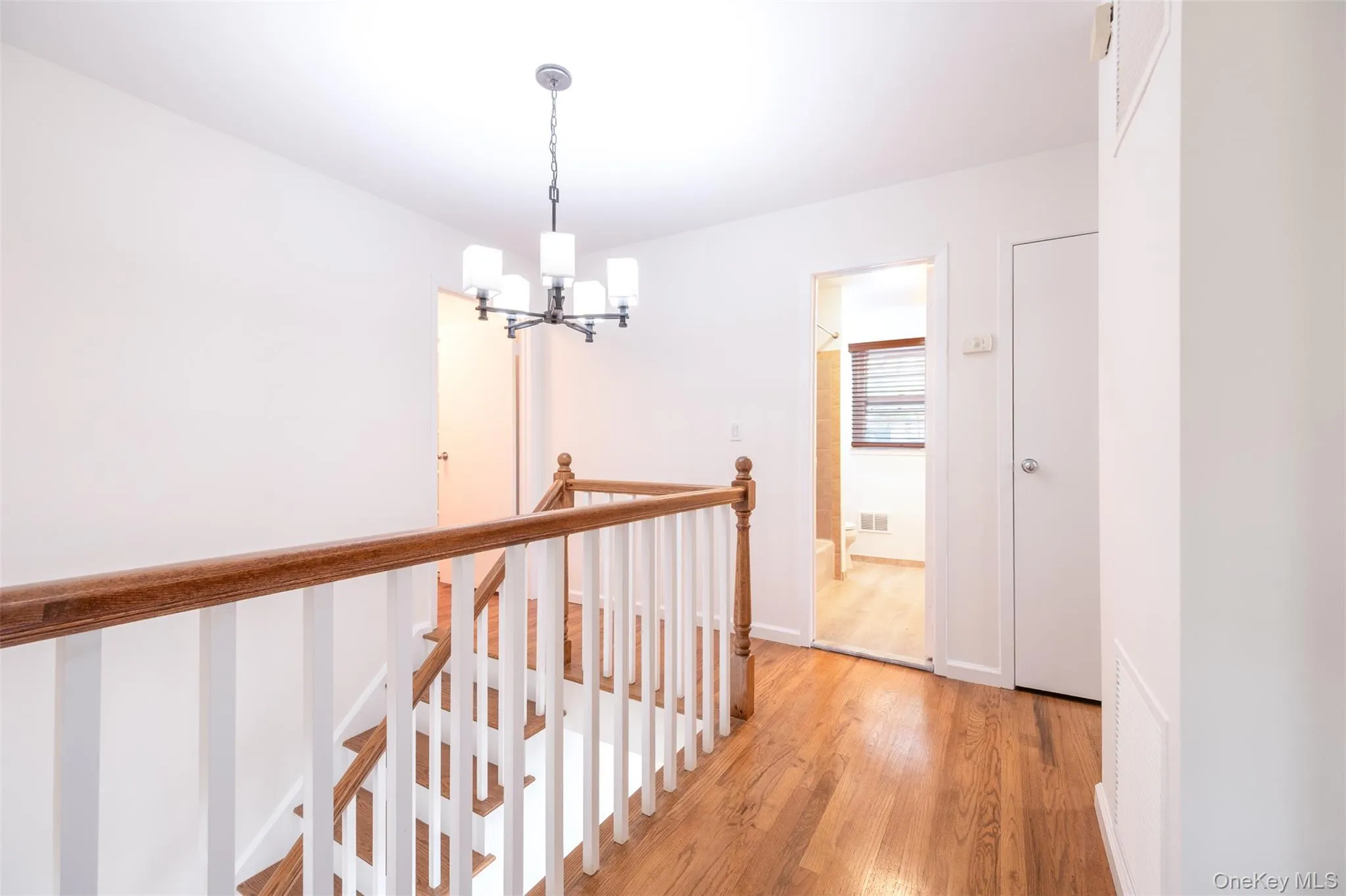 Hallway with an upstairs landing, a chandelier, and light wood finished floors Hallway with an upstairs landing, a chandelier, and light wood finished floors