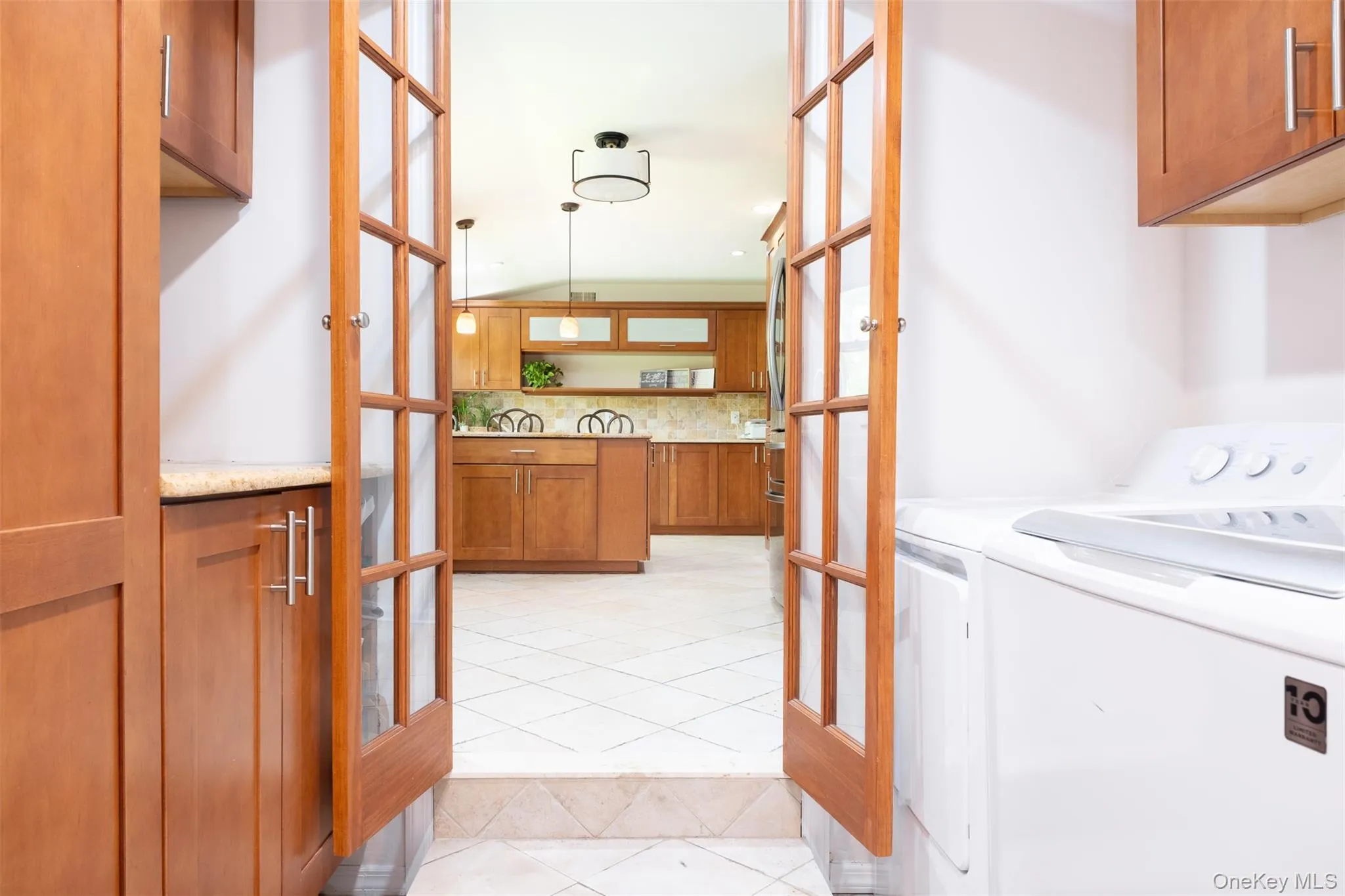 Laundry area with cabinet space, washing machine and dryer, french doors, and light tile patterned floors Laundry area with cabinet space, washing machine and dryer, french doors, and light tile patterned floors