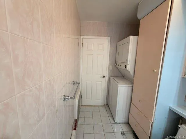 Bathroom featuring full-height tiled walls, tiled flooring, a built-in stackable washer and dryer, and integrated cabinetry Bathroom featuring full-height tiled walls, tiled flooring, a built-in stackable washer and dryer, and integrated cabinetry