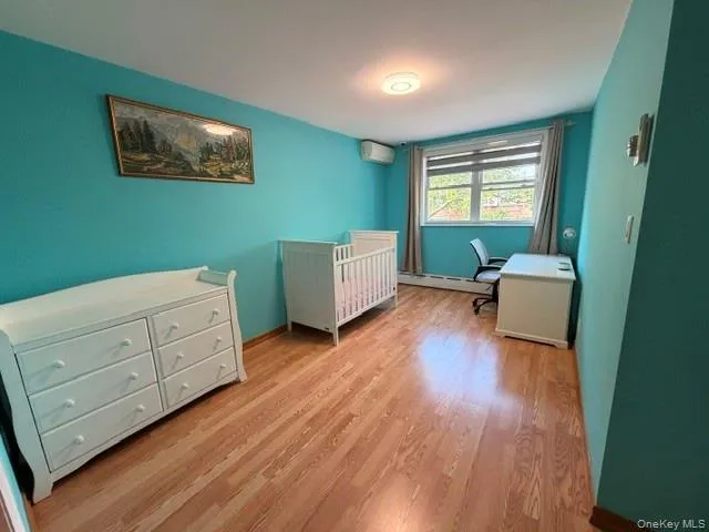 Room featuring wood-finish flooring, a window with blinds, and a ceiling-mounted light fixture Room featuring wood-finish flooring, a window with blinds, and a ceiling-mounted light fixture