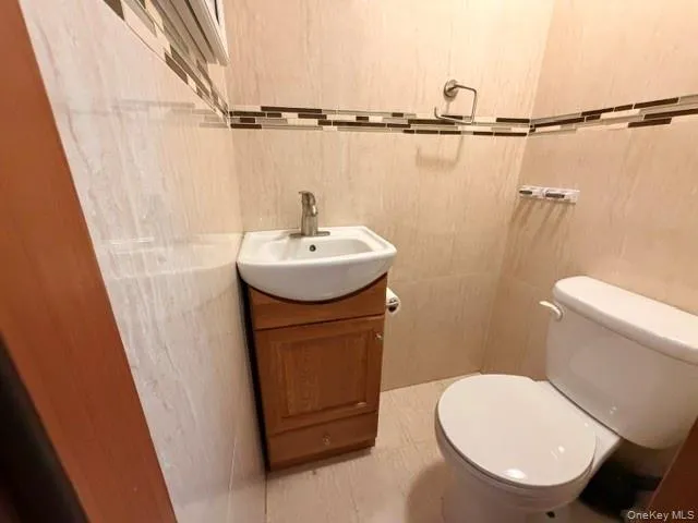 Compact bathroom featuring a white ceramic toilet and a wall-mounted sink with a wood-finish vanity Compact bathroom featuring a white ceramic toilet and a wall-mounted sink with a wood-finish vanity