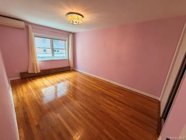 Spacious room featuring wood-finish flooring, a window with natural light, and a decorative ceiling light fixture Spacious room featuring wood-finish flooring, a window with natural light, and a decorative ceiling light fixture