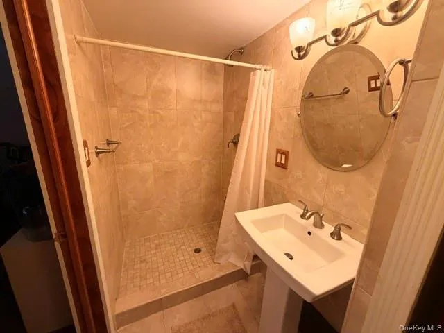 Bathroom featuring a pedestal sink, round mirror, and a three-light vanity fixture Bathroom featuring a pedestal sink, round mirror, and a three-light vanity fixture