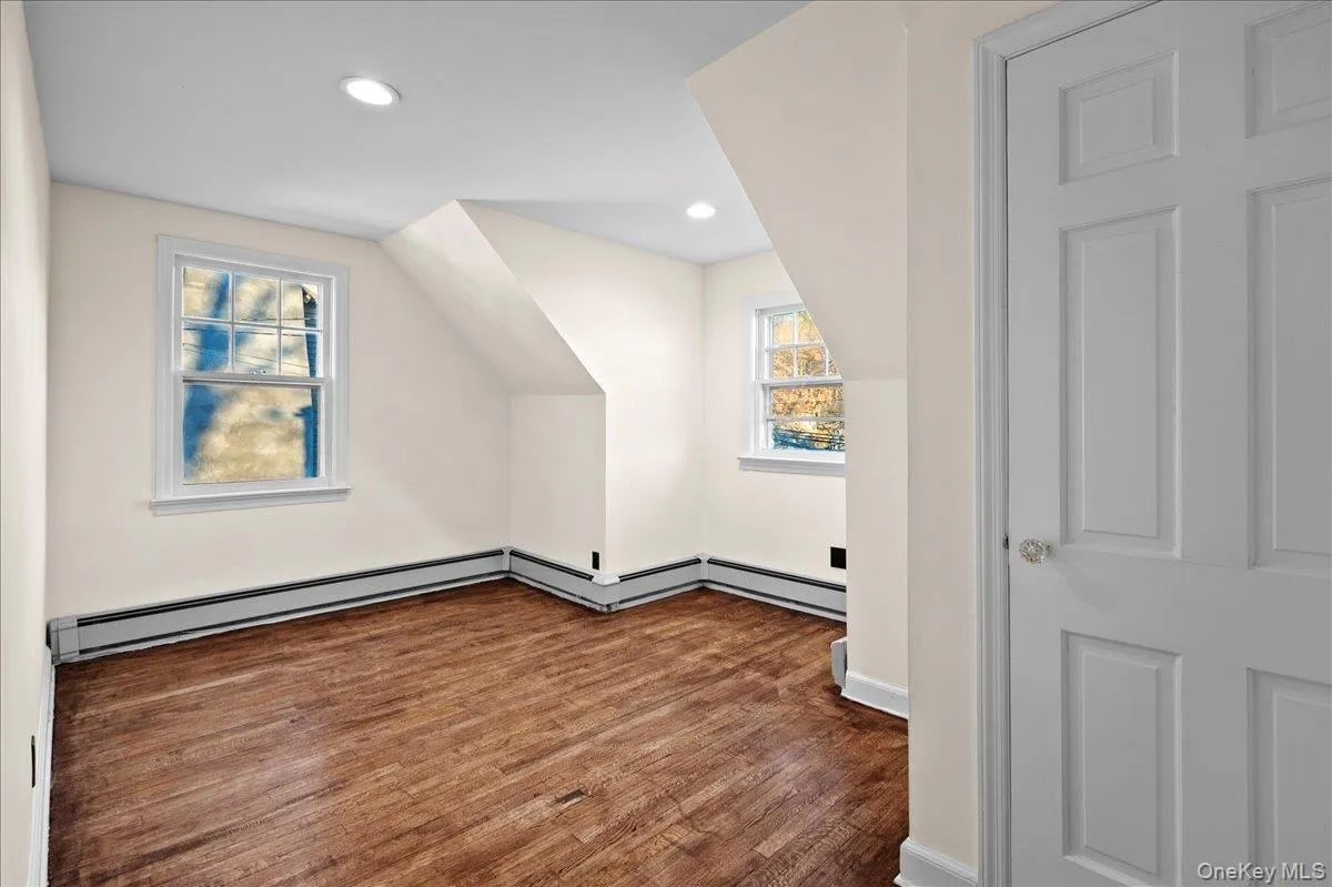 Attic room featuring wood-finish flooring, two windows with white trim, and recessed ceiling lighting Attic room featuring wood-finish flooring, two windows with white trim, and recessed ceiling lighting