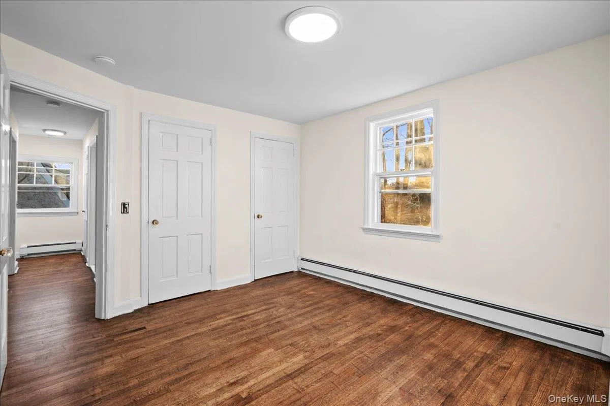 Room featuring wood-finish flooring, neutral wall paint, and a large window providing ambient light Room featuring wood-finish flooring, neutral wall paint, and a large window providing ambient light