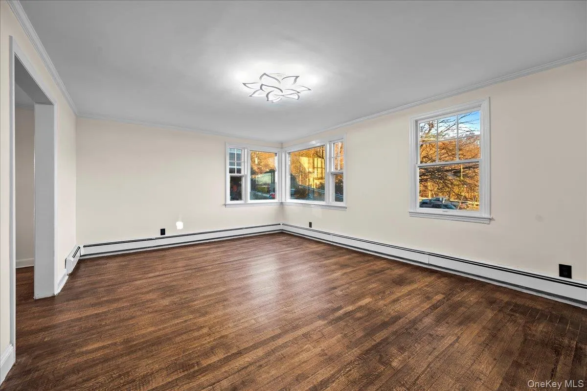 Spacious room featuring wood-finish flooring, white baseboard trim, and crown molding Spacious room featuring wood-finish flooring, white baseboard trim, and crown molding
