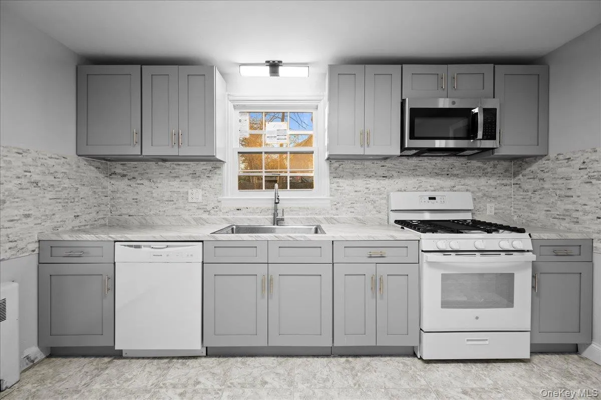Modern kitchen featuring gray shaker-style cabinetry, a stacked stone-look backsplash, and light-toned countertops Modern kitchen featuring gray shaker-style cabinetry, a stacked stone-look backsplash, and light-toned countertops