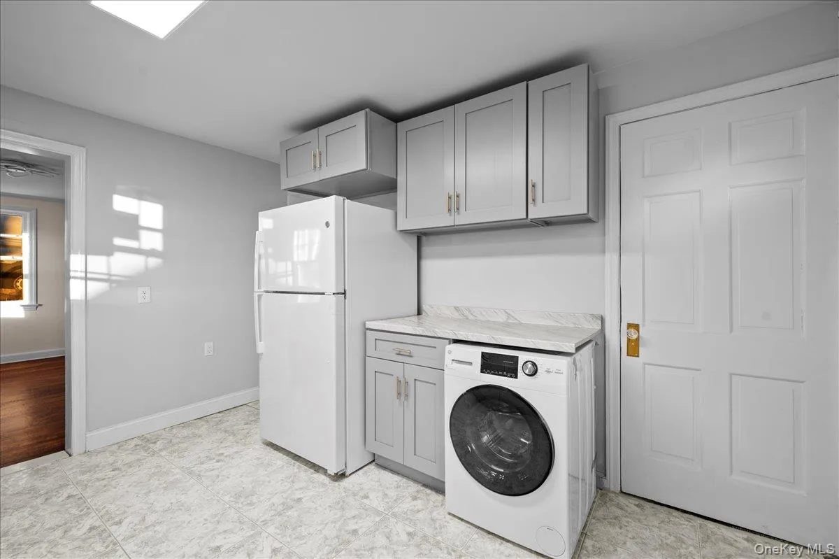Laundry area featuring a front-load washer, light gray cabinetry, and a white countertop Laundry area featuring a front-load washer, light gray cabinetry, and a white countertop