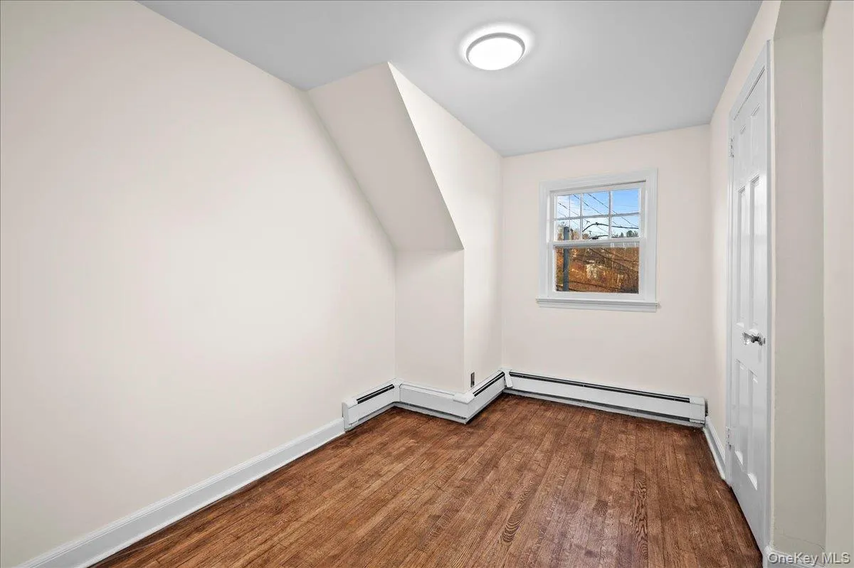 Room featuring wood-finish flooring, white baseboards, and neutral wall paint Room featuring wood-finish flooring, white baseboards, and neutral wall paint